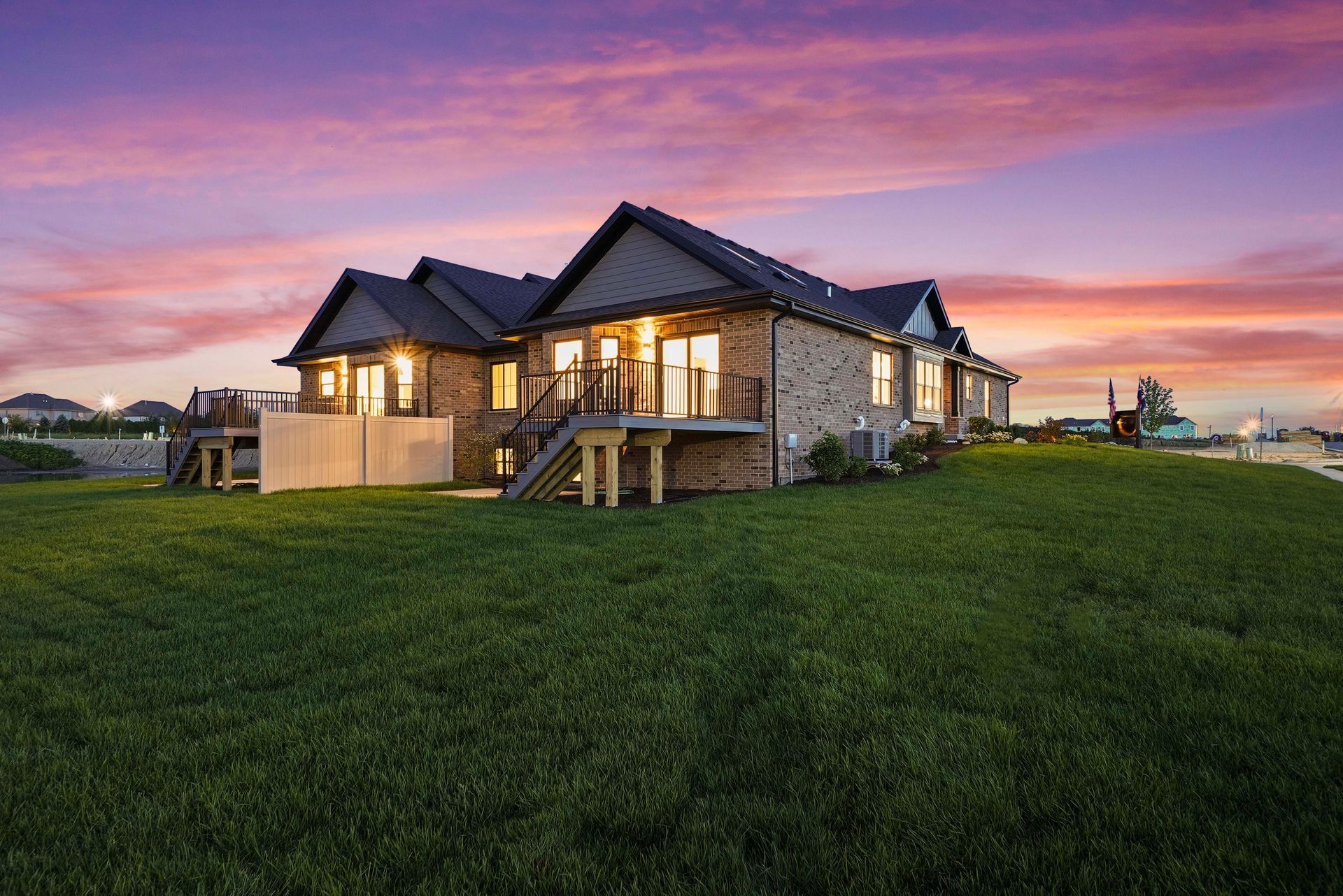 Modern stone house at sunset with warm lights and a large green lawn