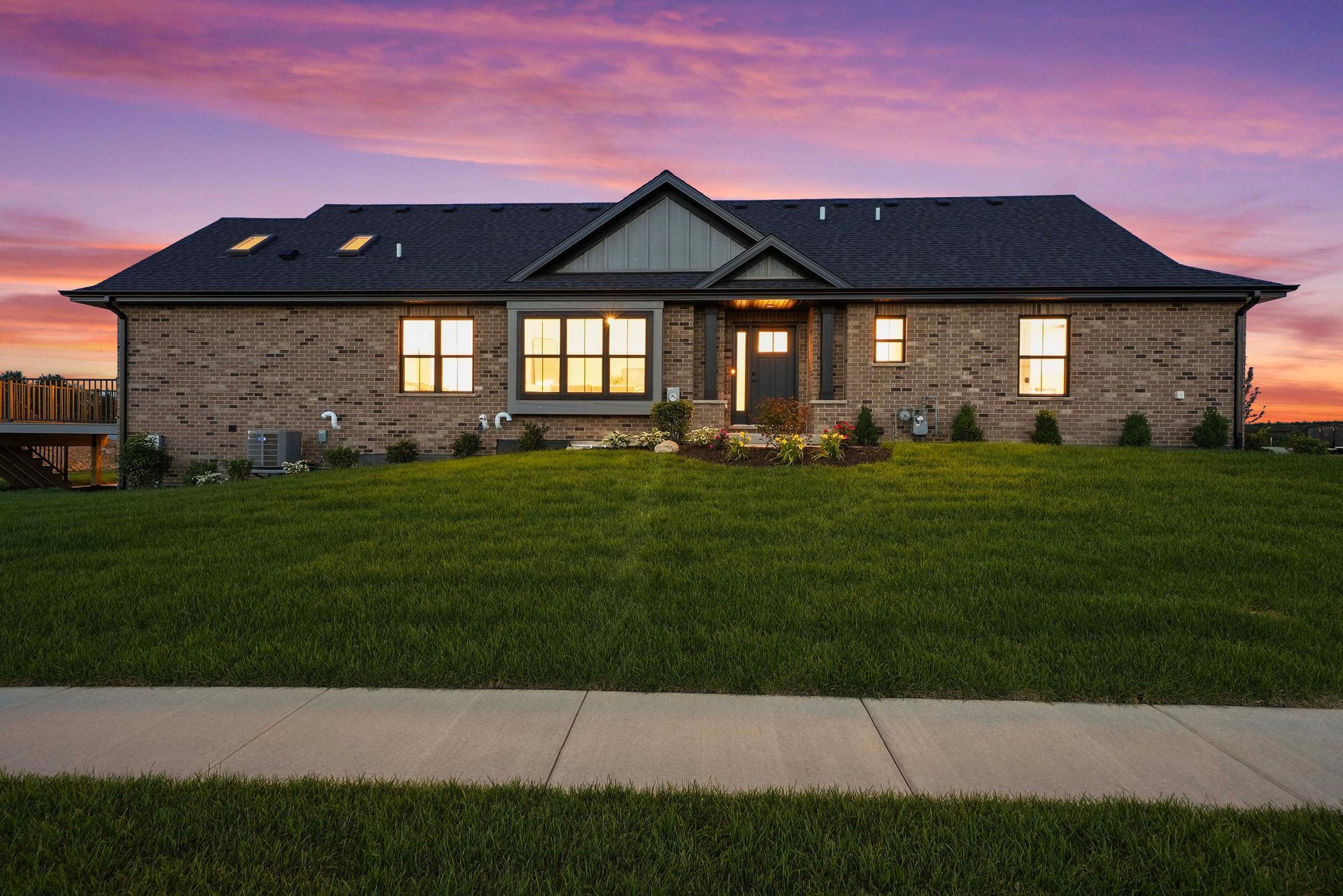 Single-story brick house at dusk with lit windows and a purple sunset sky