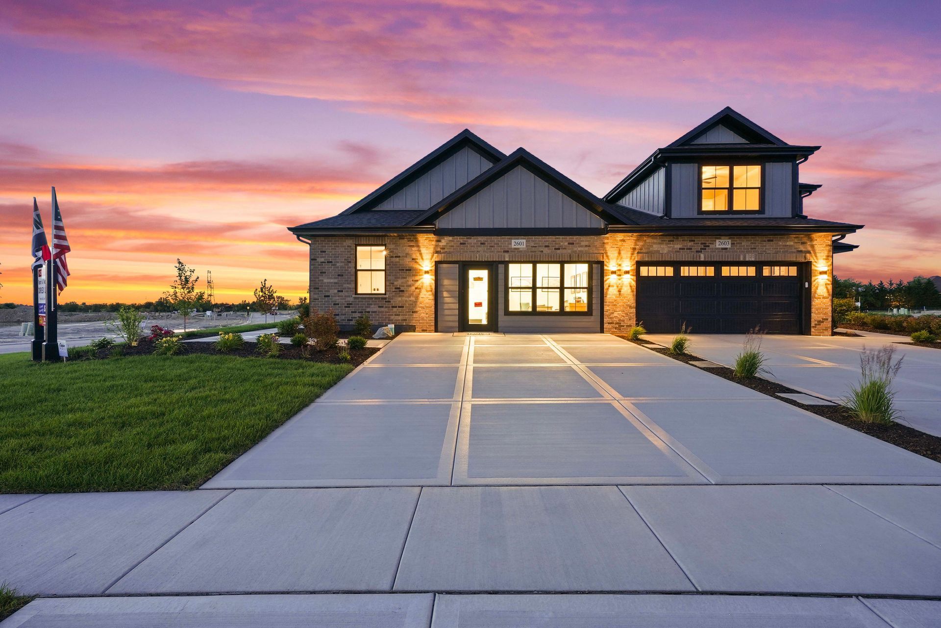 Modern two-story house with stone accents and a long driveway at sunset