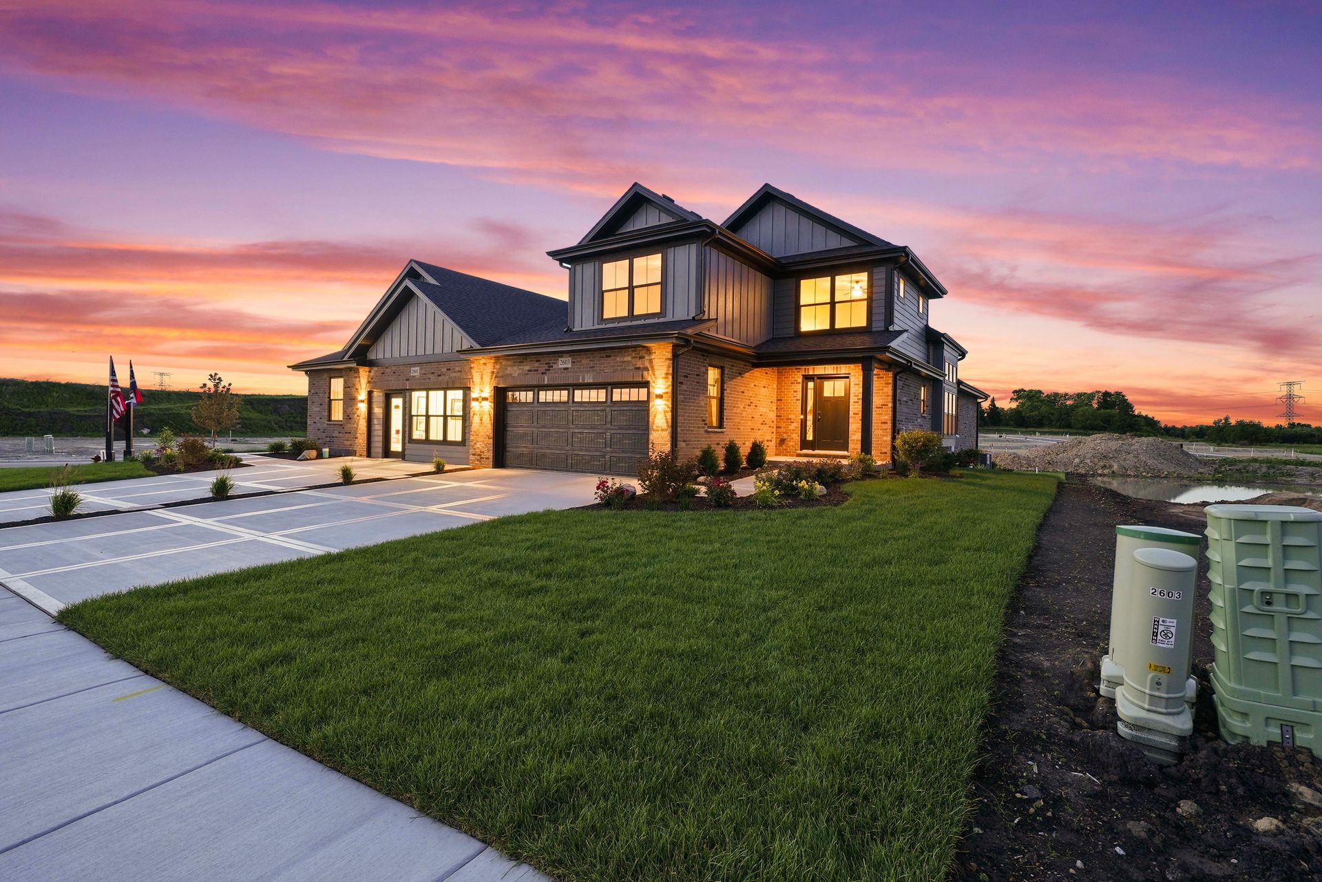 Modern two-story house with stone accents at sunset, front lawn, driveway, and pink-purple sky