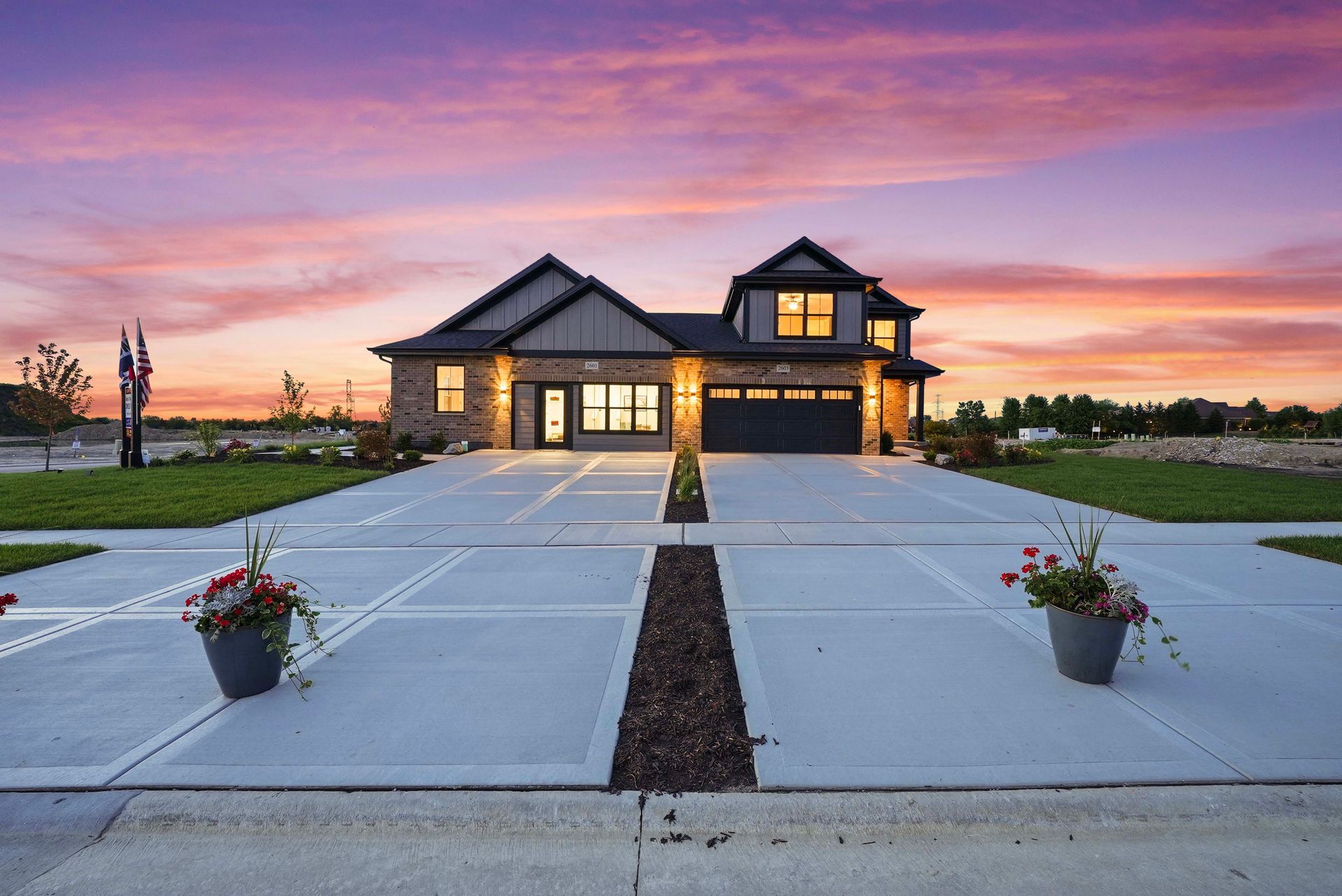 Modern two-story house at sunset with a lit entry and flower pots lining the driveway