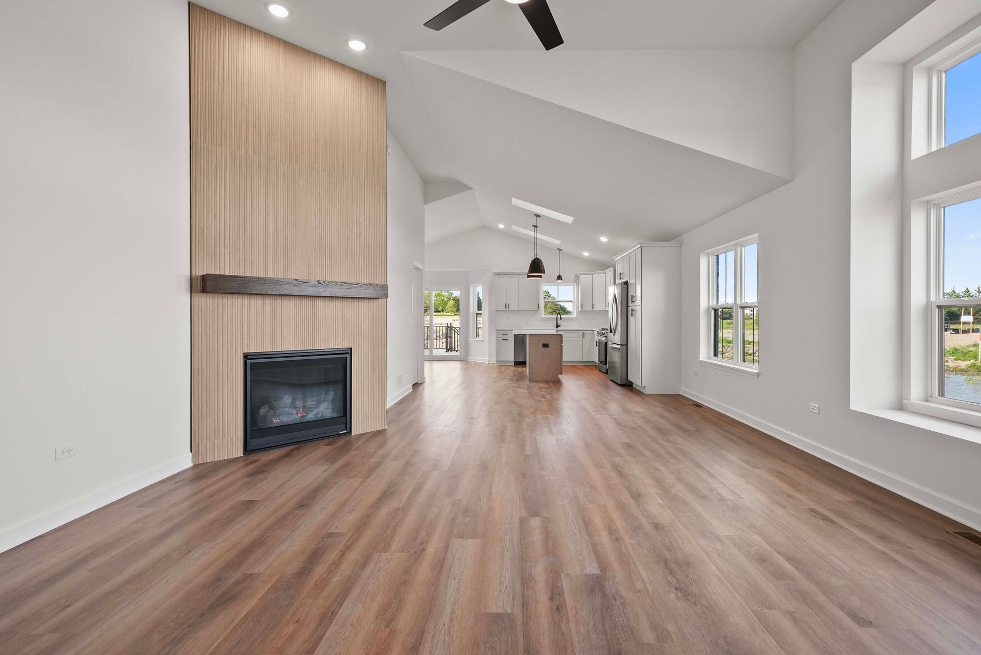 Empty modern living room with wood floors, white walls, a fireplace, and tall windows