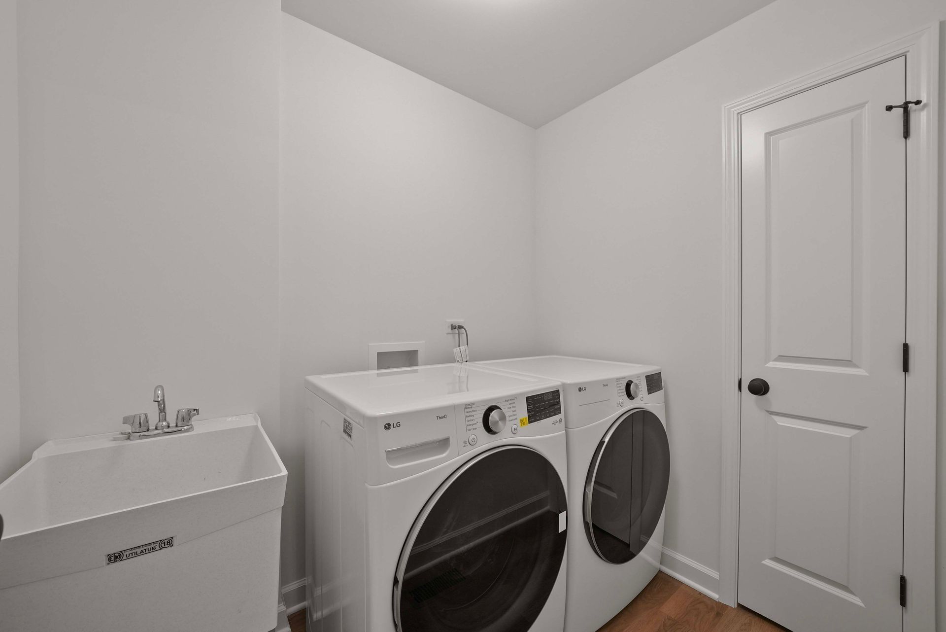 Laundry room with a white washer and dryer, utility sink, and closed door on the right.