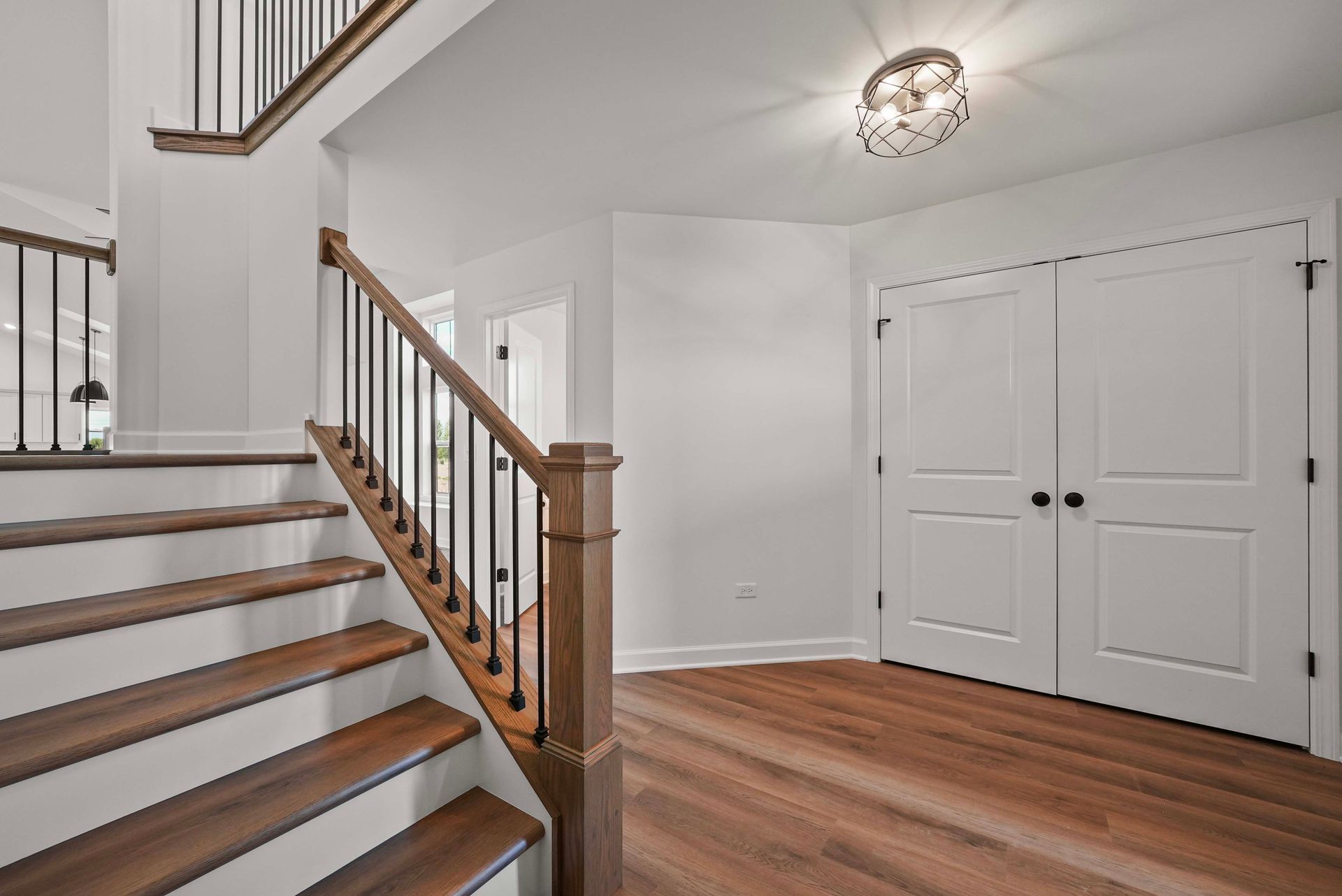 Bright foyer with wooden staircase, white double doors, and hardwood floors.