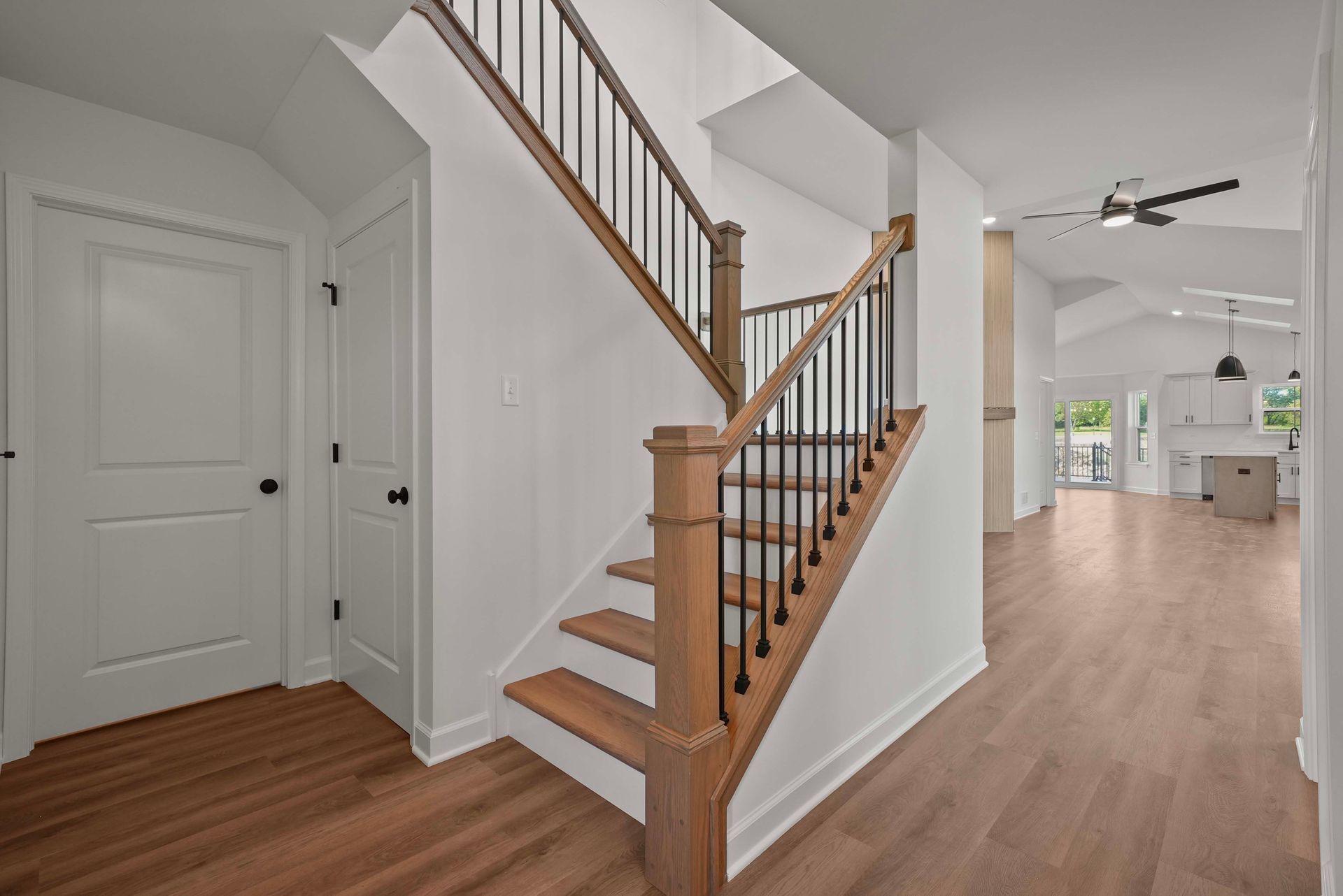 Staircase with wood railings in a bright open foyer leading to a kitchen and living area