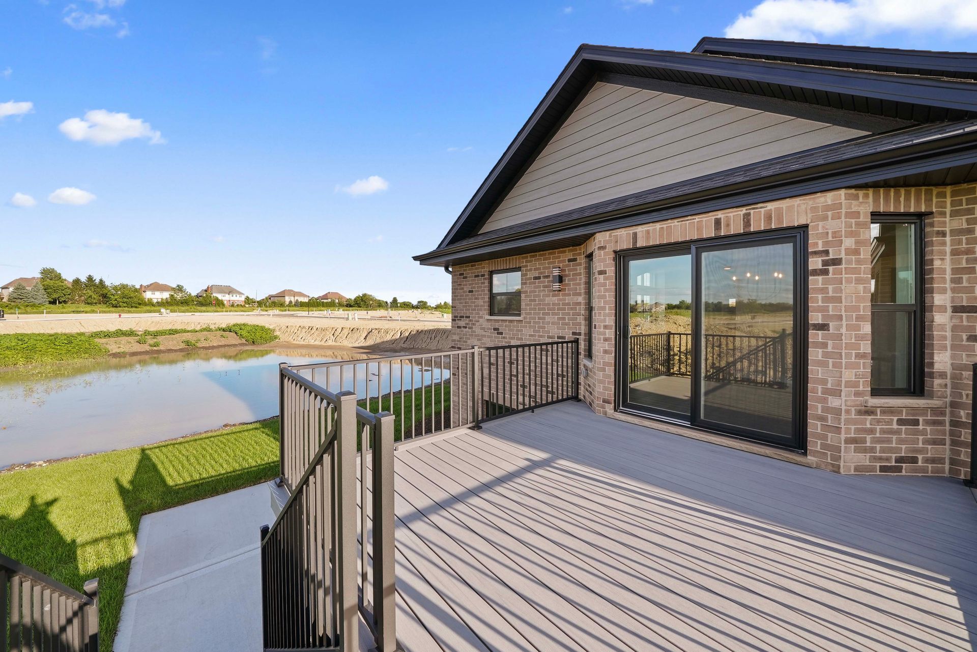 Patio deck with sliding glass doors overlooking a pond and green lawn under a blue sky