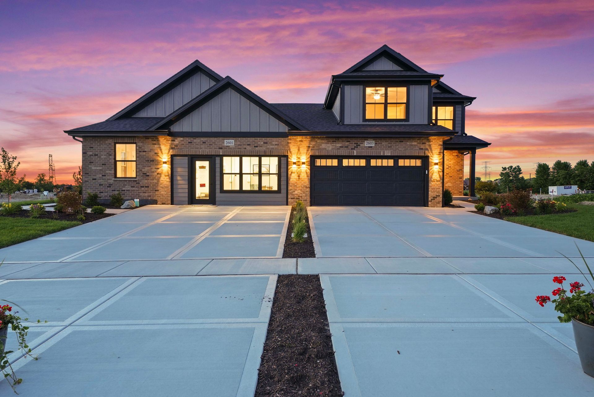 Modern two-story house with stone exterior, large driveway, and lit windows at sunset