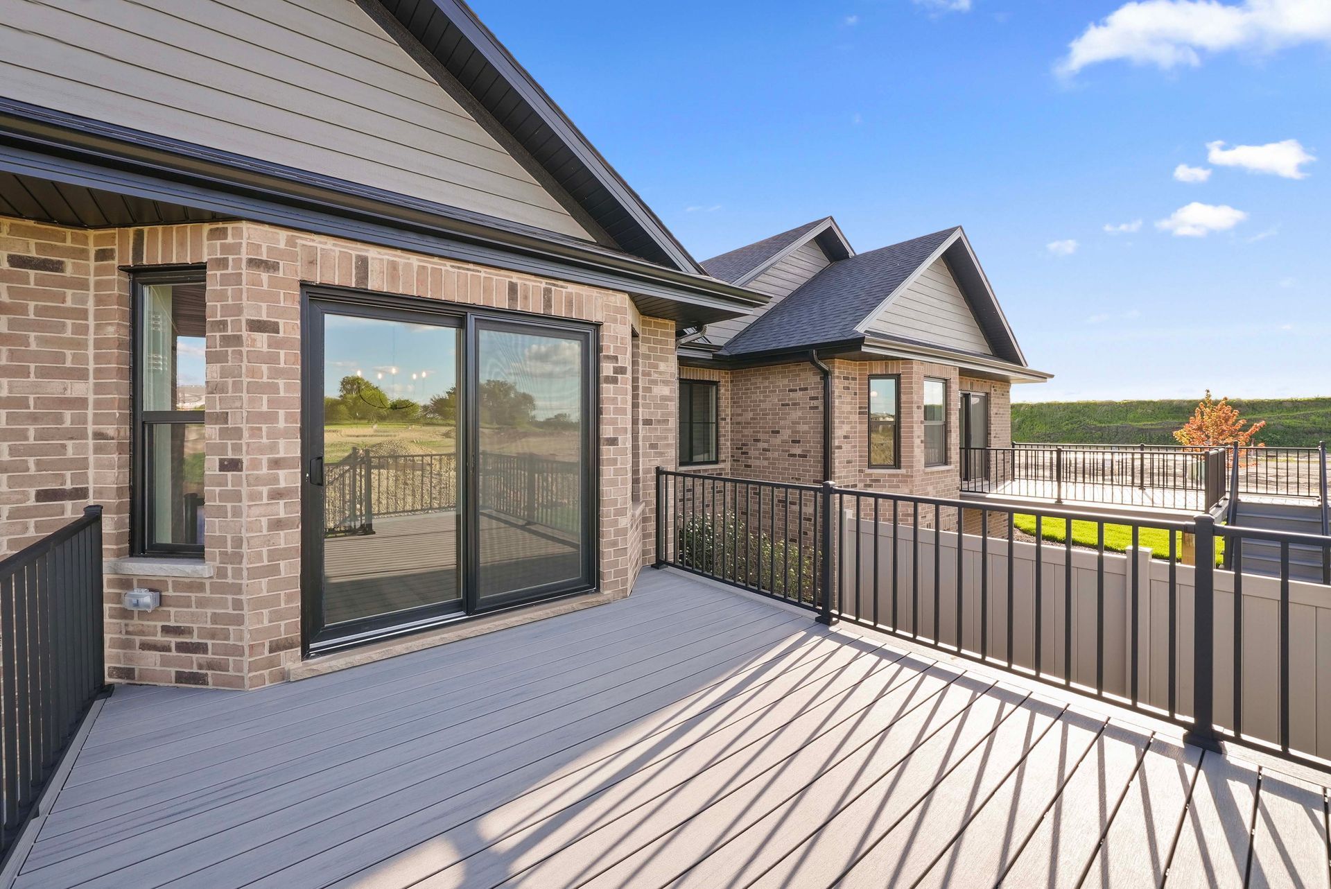 Modern brick house deck with black railings and large sliding glass doors under a blue sky