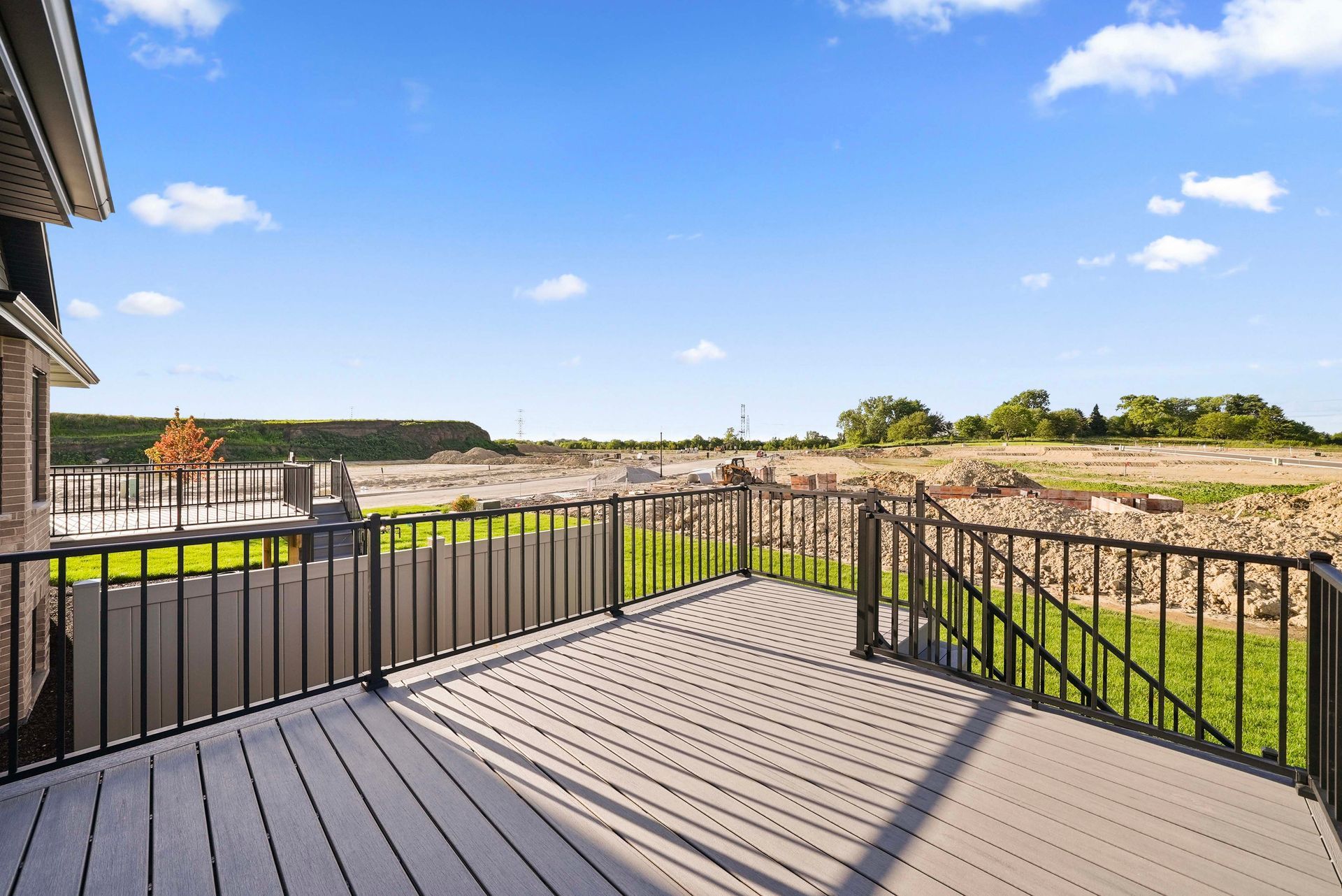 Wooden deck with black railing overlooking a grassy landscape under a bright blue sky