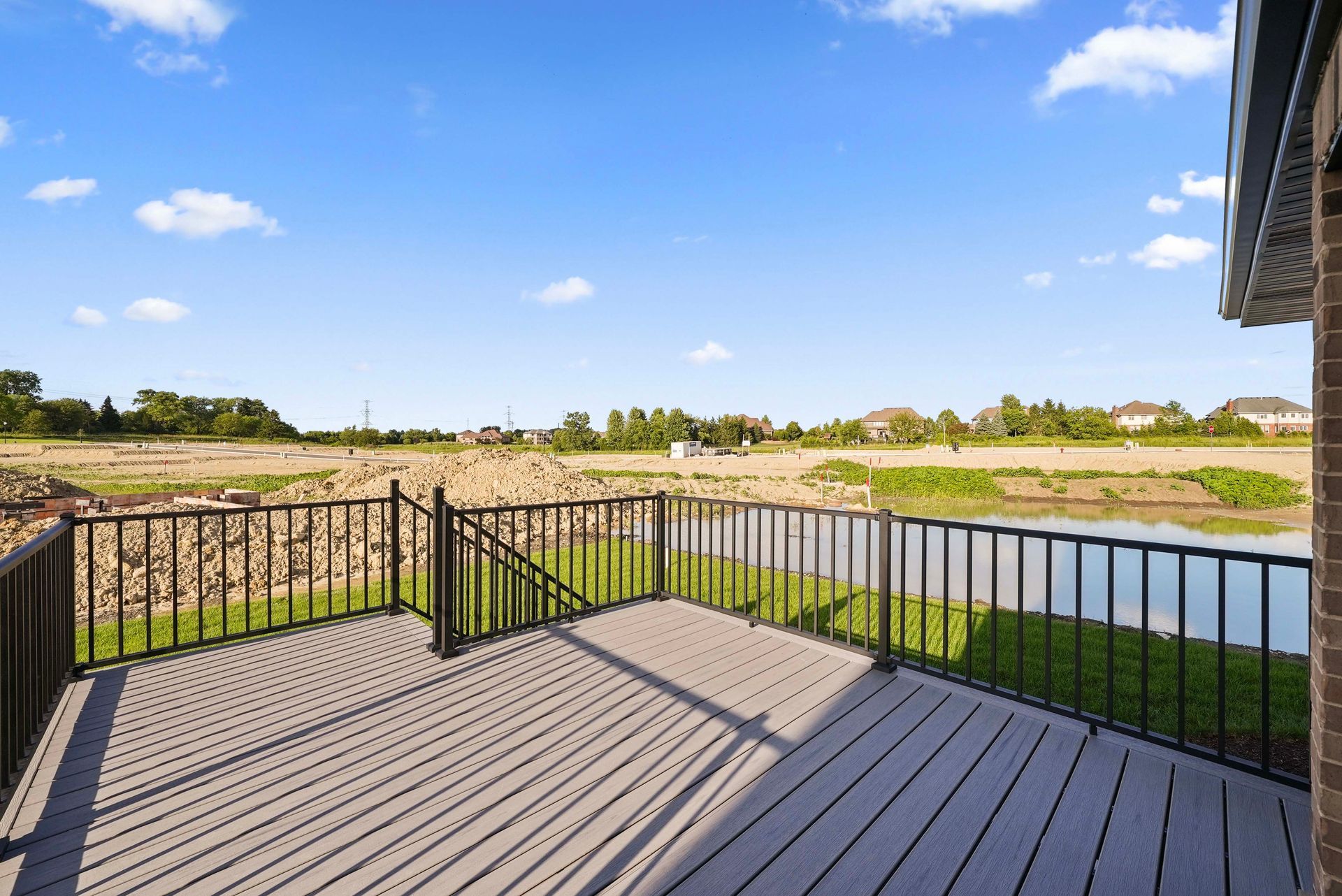 Deck overlooking a pond and grassy field under a blue sky