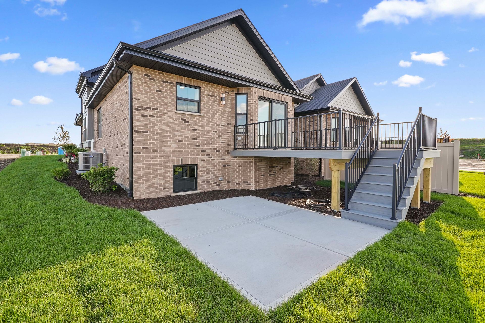 Brick house exterior with raised deck, concrete patio, and stairs in a grassy yard.