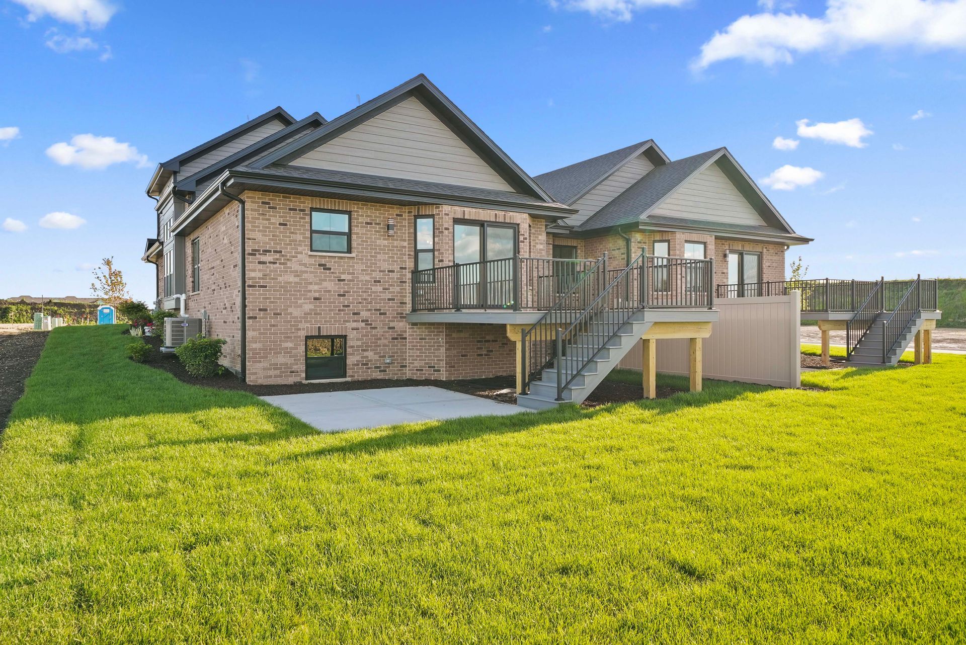 Modern brick house with a deck and balcony, set beside a large green lawn under a blue sky