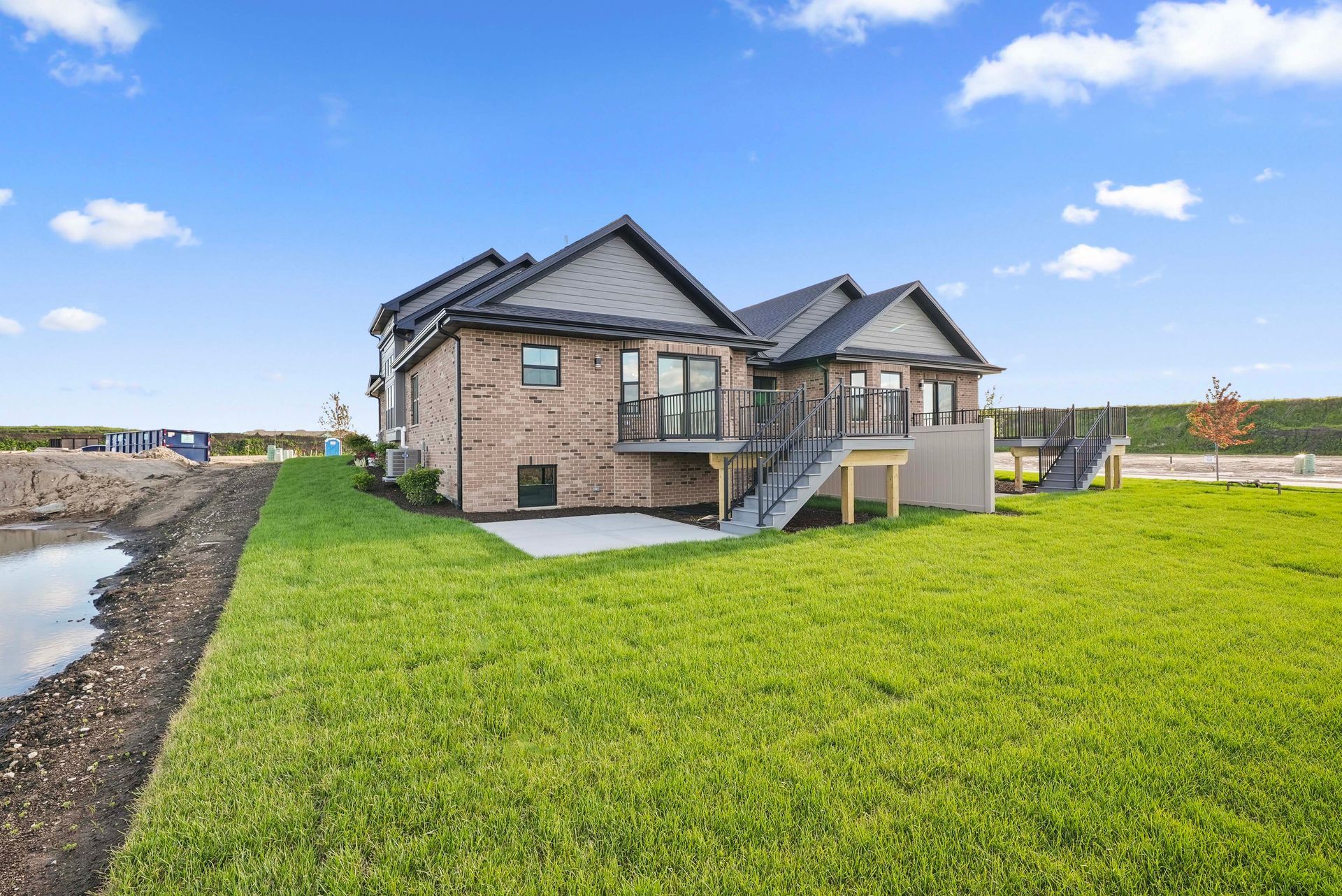 Modern brick house with gray roof and large green lawn under a blue sky