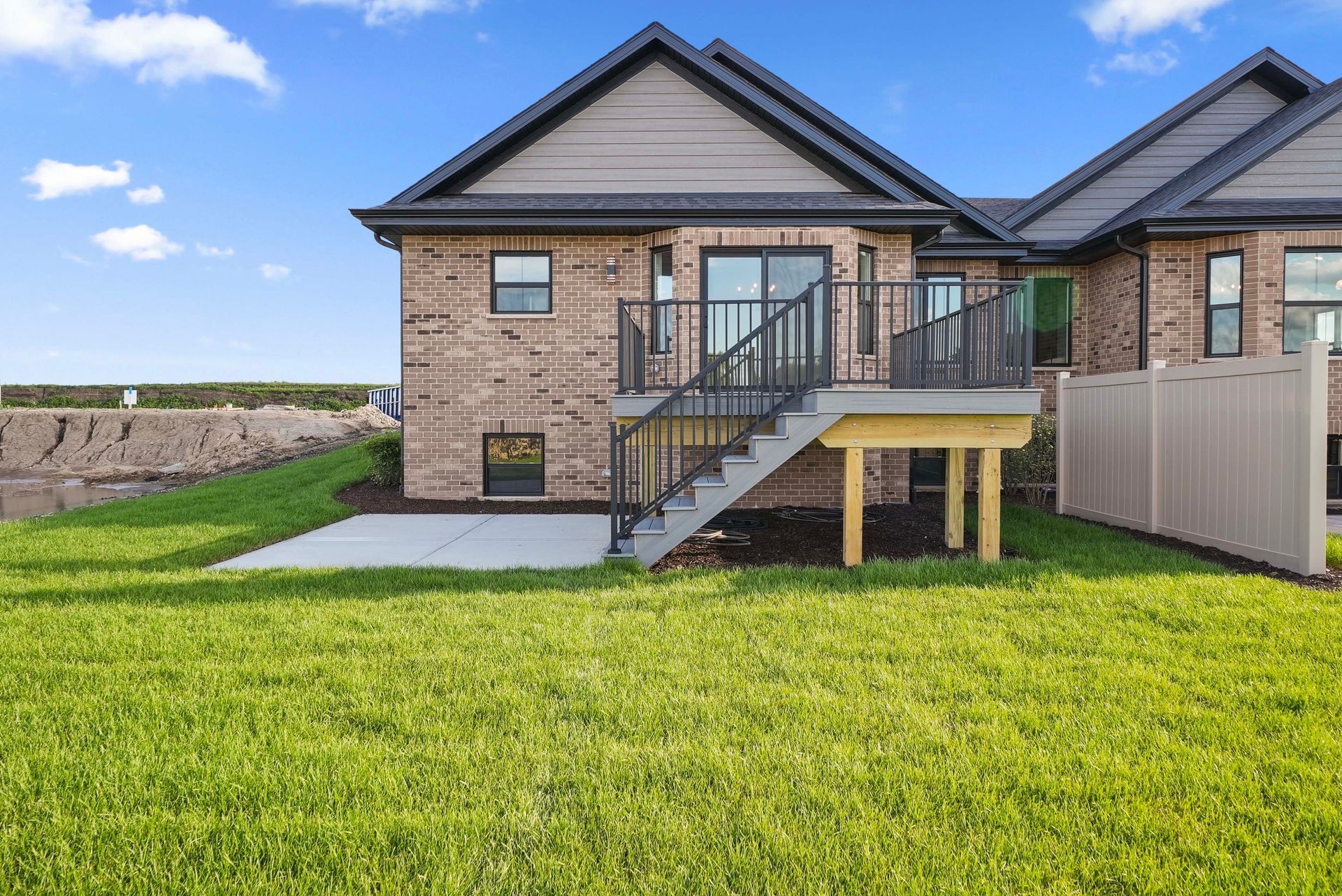 Brick house exterior with raised deck, stairs, and a green backyard lawn