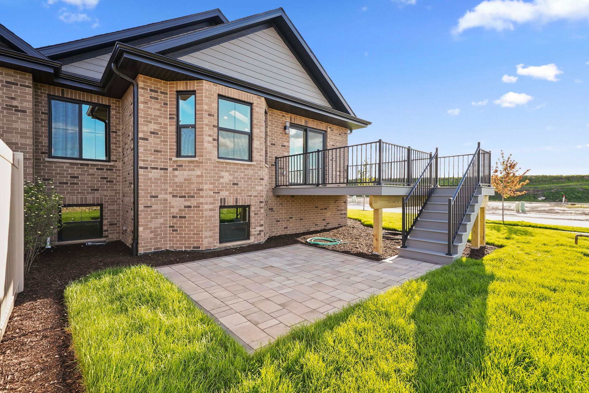 Brick house with raised deck and stairs, overlooking a grassy yard and paved patio.