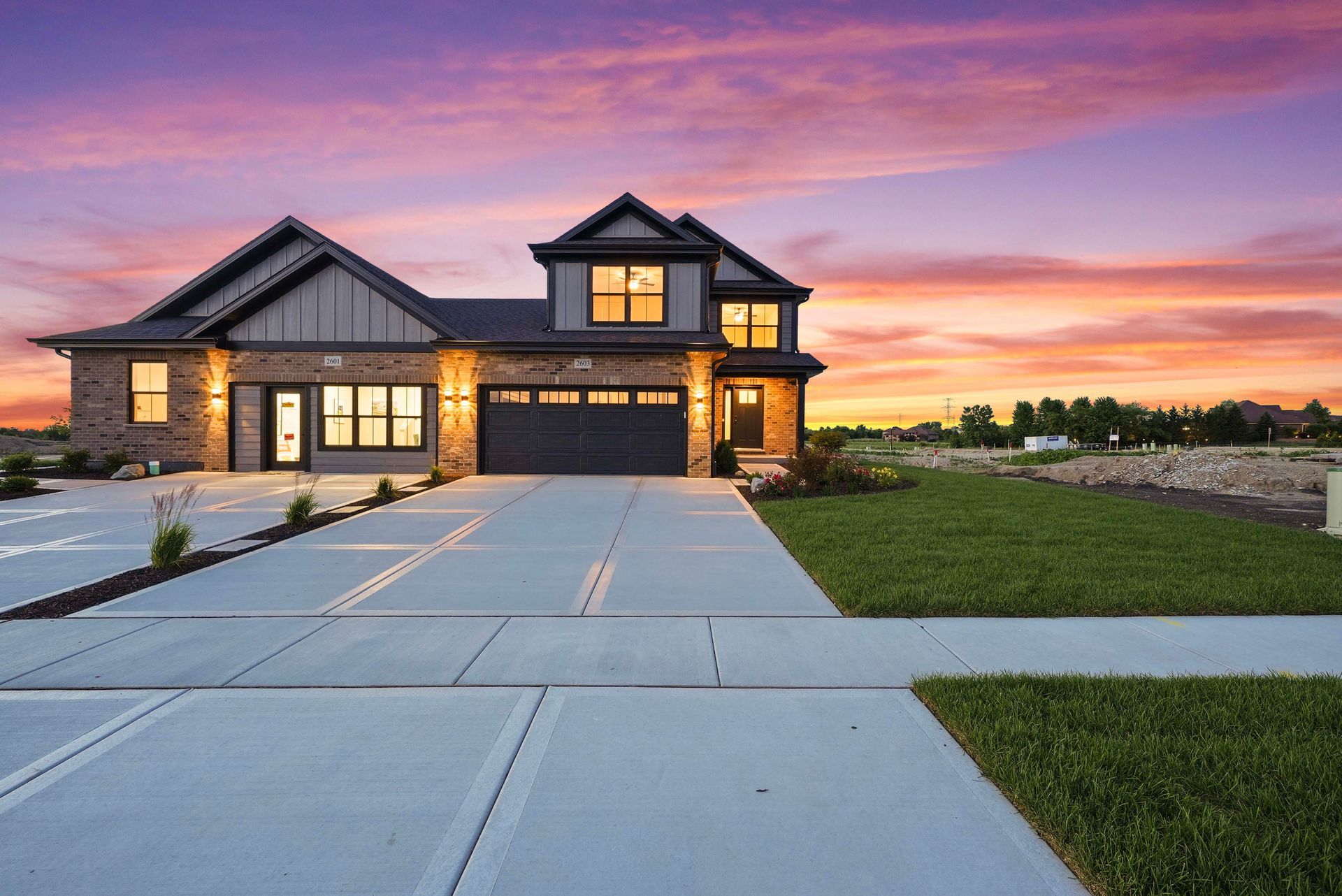 Modern suburban house with a lit exterior at sunset and a wide concrete driveway