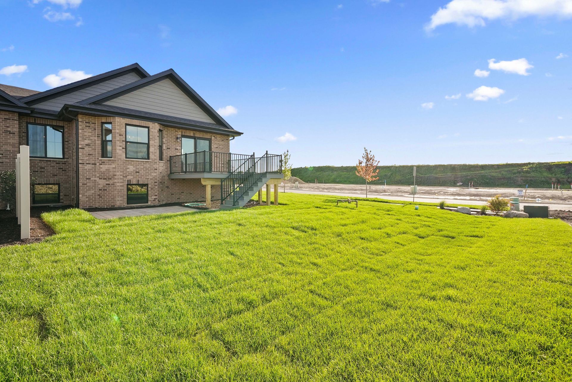 Brick house with a large green lawn and wooden deck overlooking a cloudy landscape