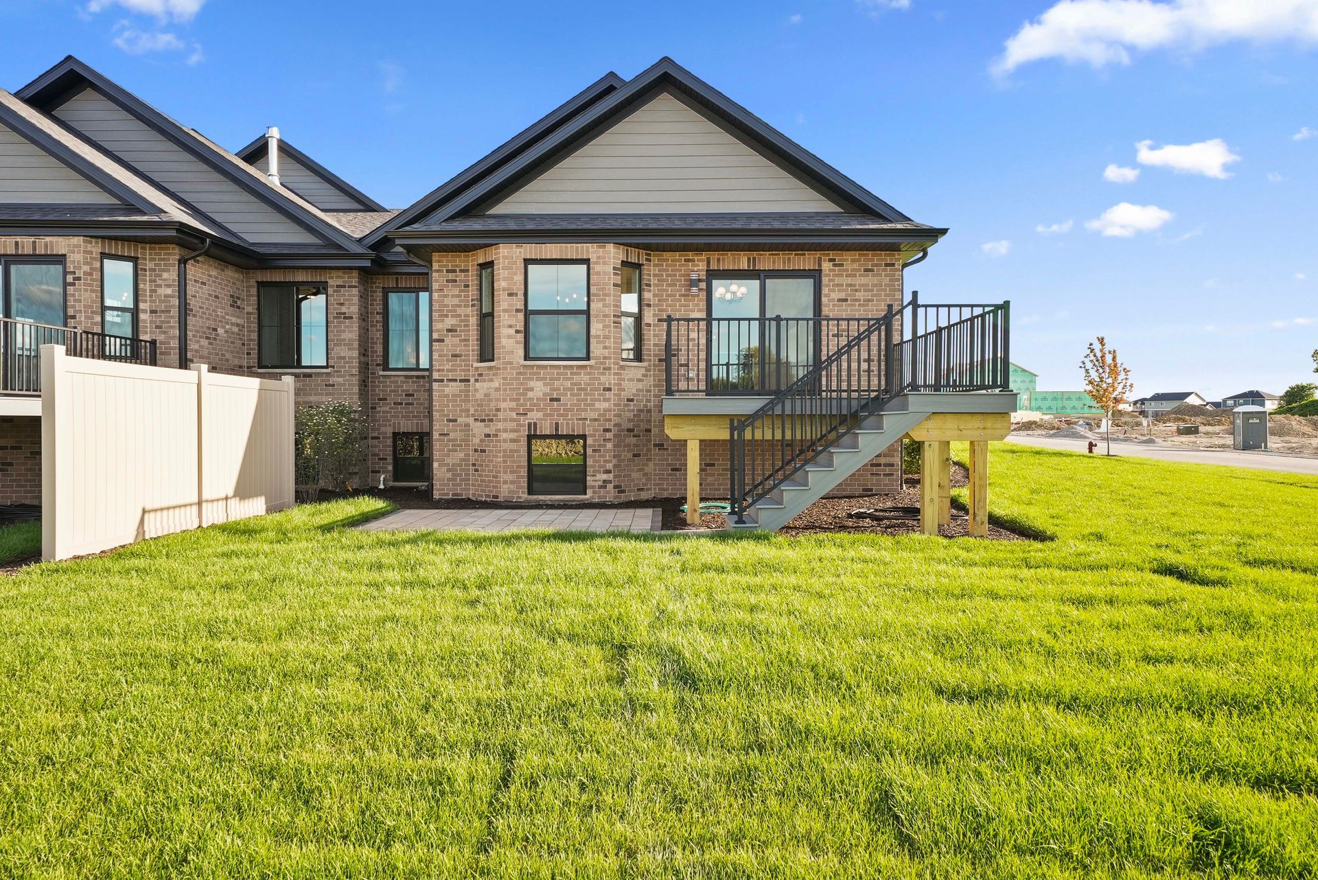 Brick house with a raised deck and stairs, set beside a bright green lawn under a blue sky.