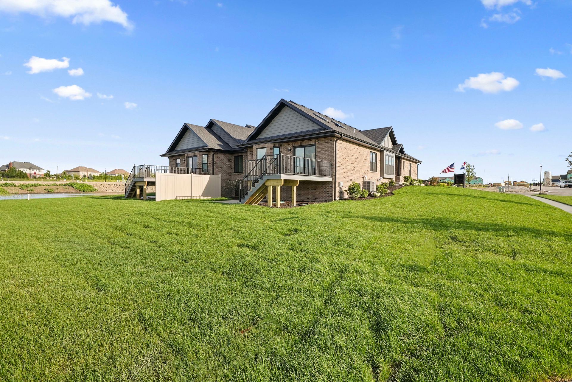Large modern stone house with a balcony on a grassy field under a blue sky