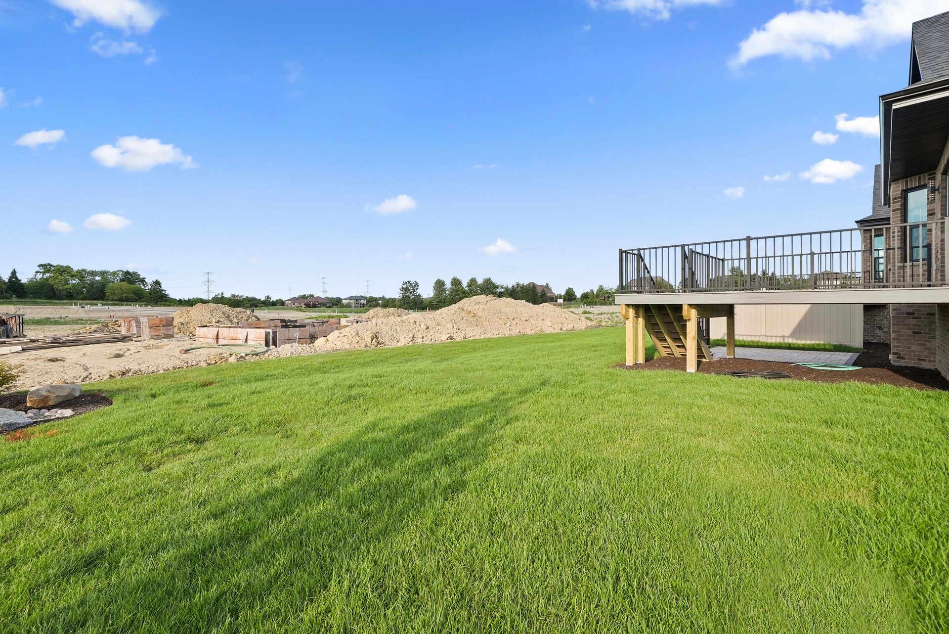 Green lawn beside a patio deck overlooking a sandy construction site under a blue sky