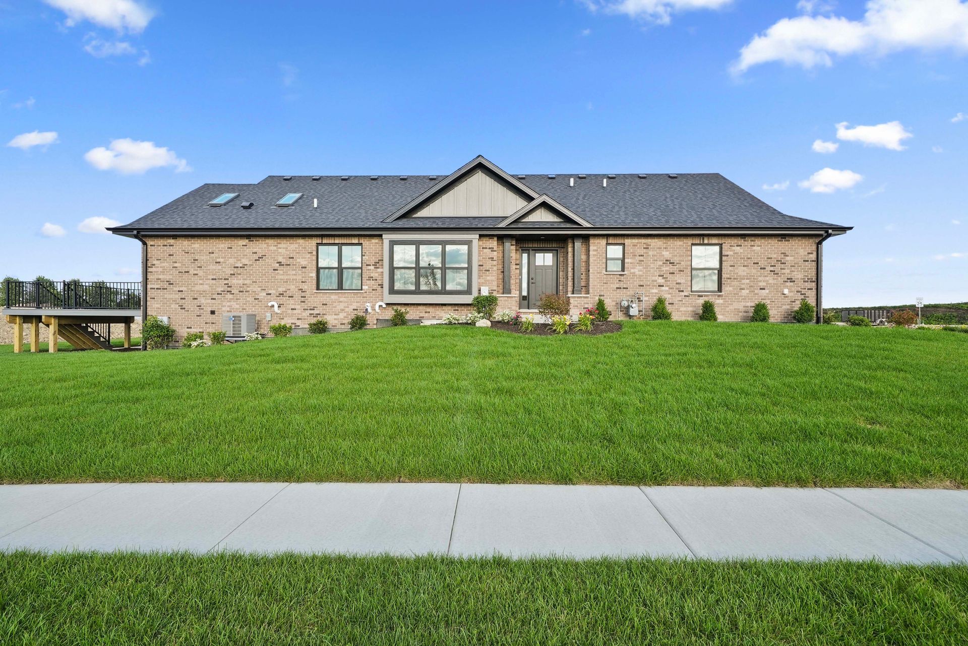 Single-story brick house with gray roof and front lawn under a blue sky