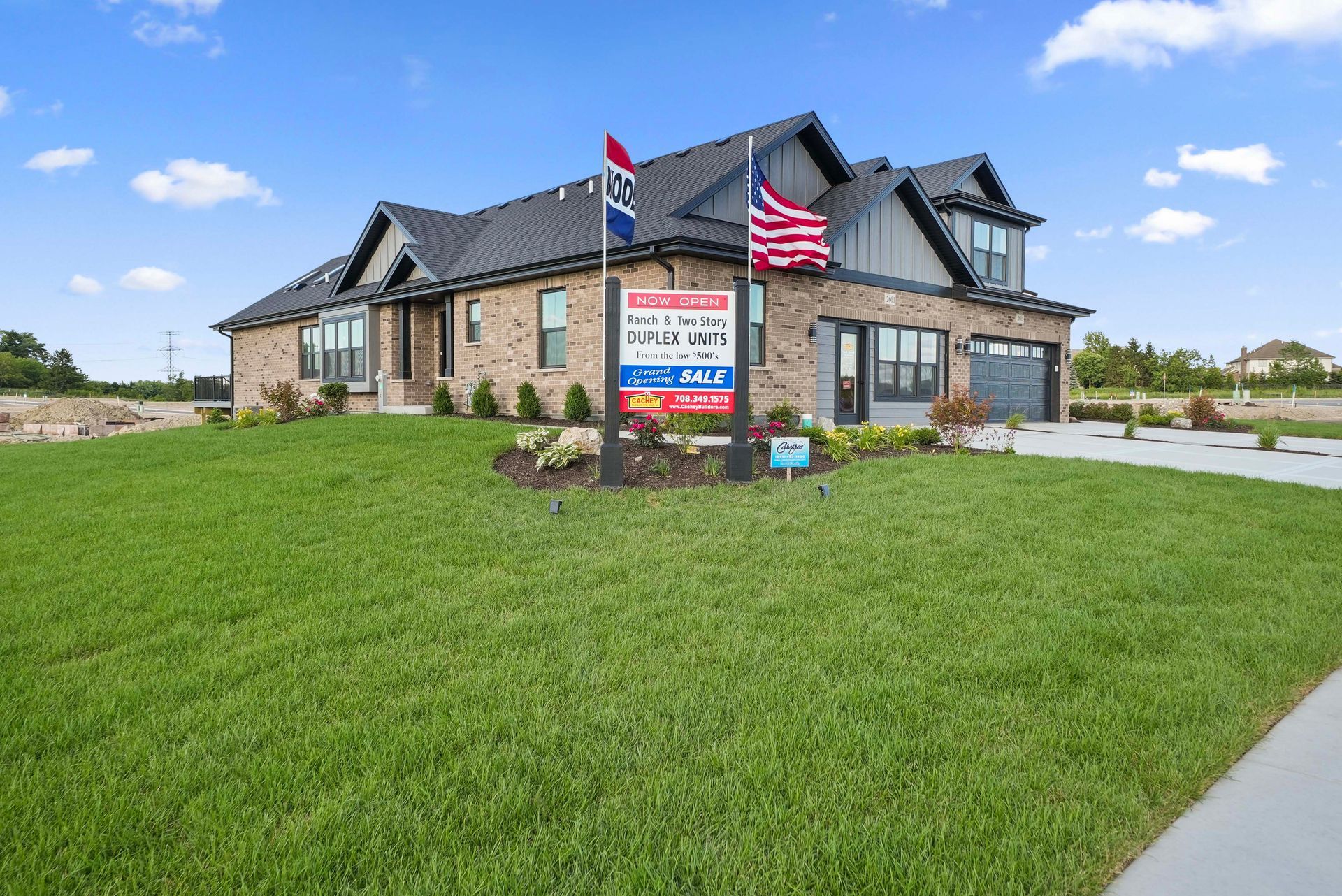 Stone commercial building with American flag and red-white-blue sign on a green lawn under a blue sky