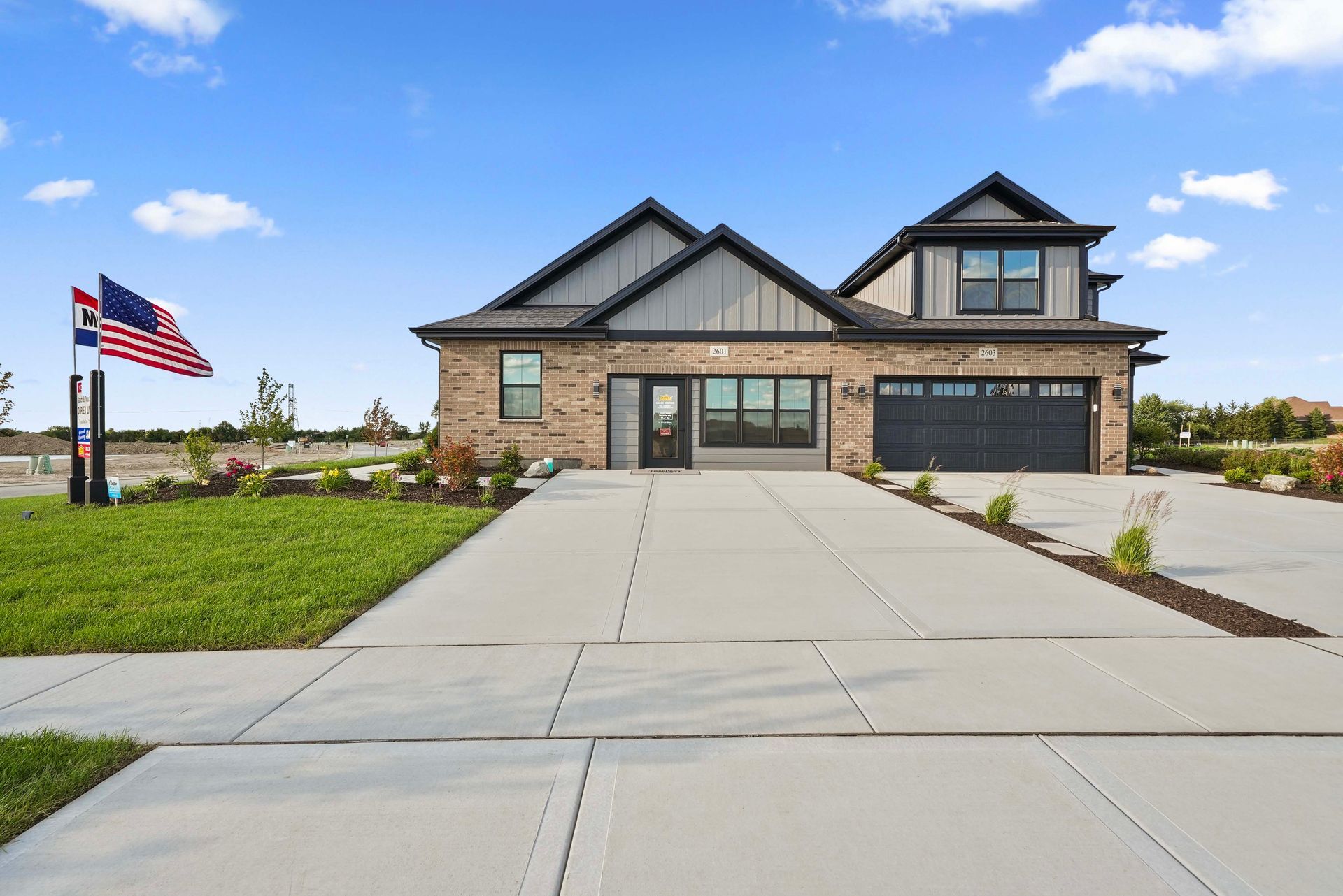 Modern two-story suburban house with a wide driveway and American flag on a lawn under a blue sky