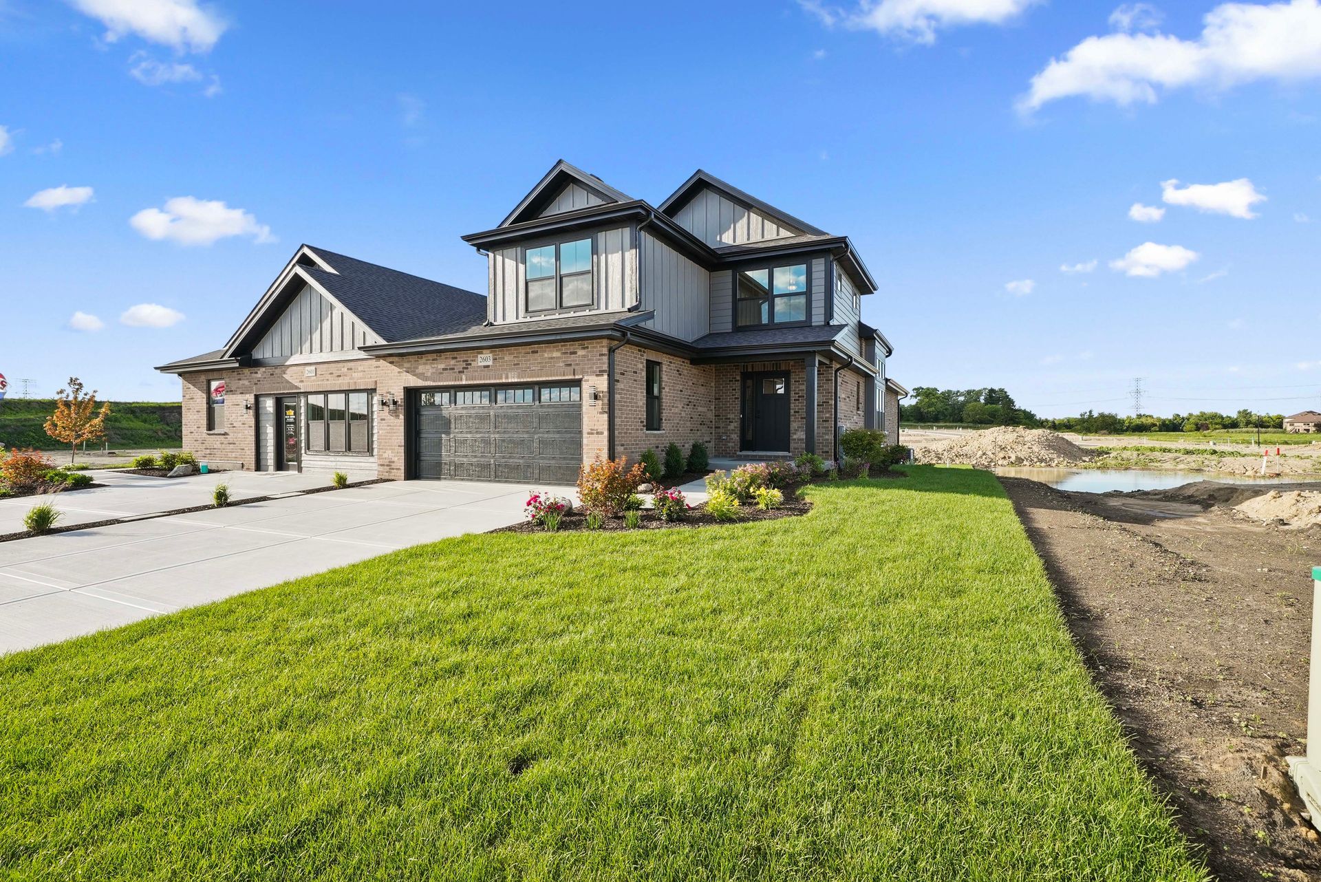 Modern two-story stone house with a large driveway and green lawn under a blue sky