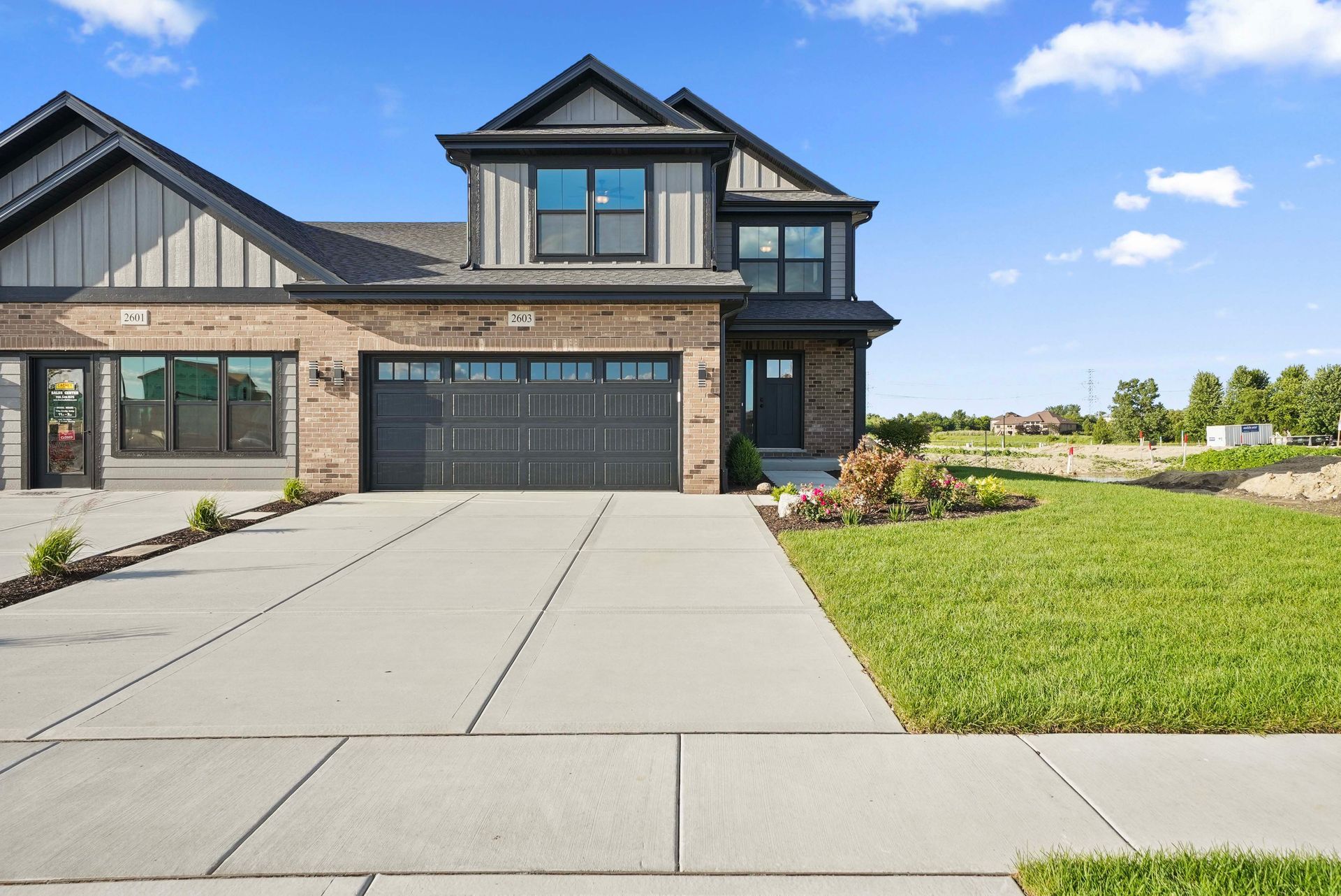 Modern two-story house with gray siding, black garage, and a large concrete driveway under a blue sky