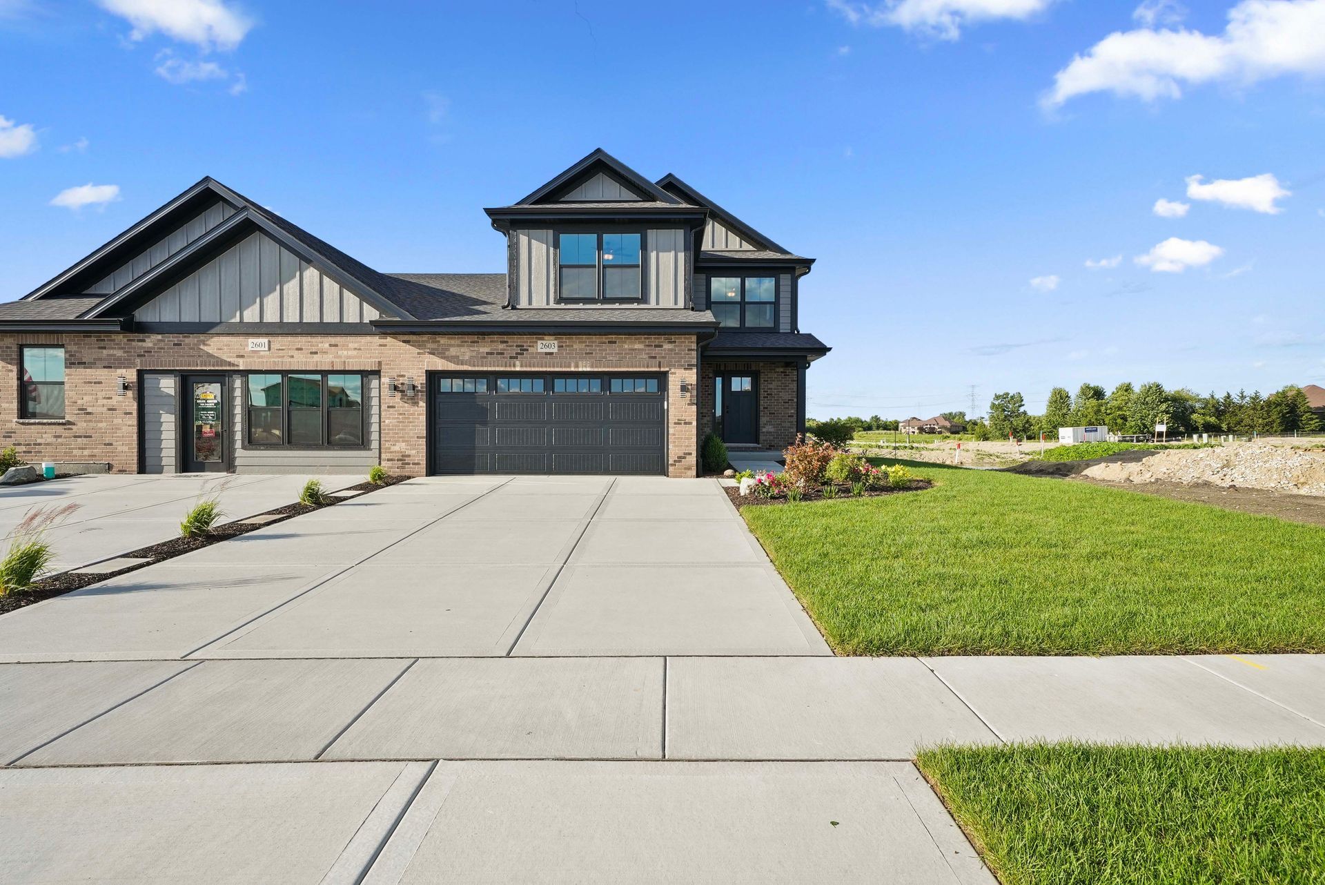Modern two-story brick house with a large concrete driveway and green lawn under a blue sky