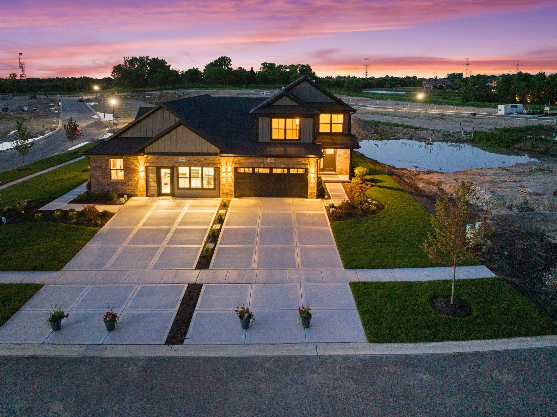 Modern two-story house with lit windows and a long driveway at dusk by a lake
