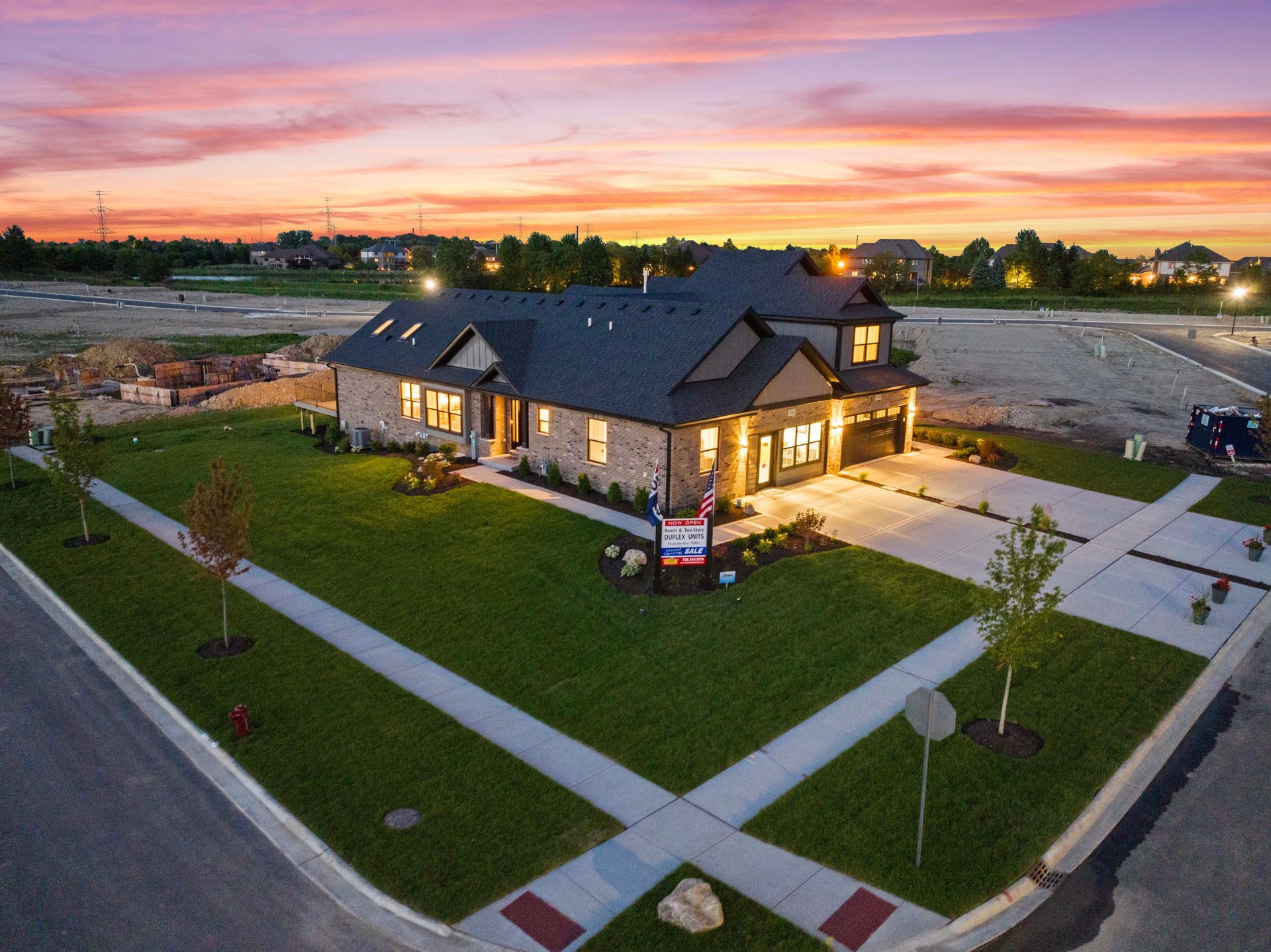 Newly built house at dusk with warm lights, green lawn, and pink sunset sky