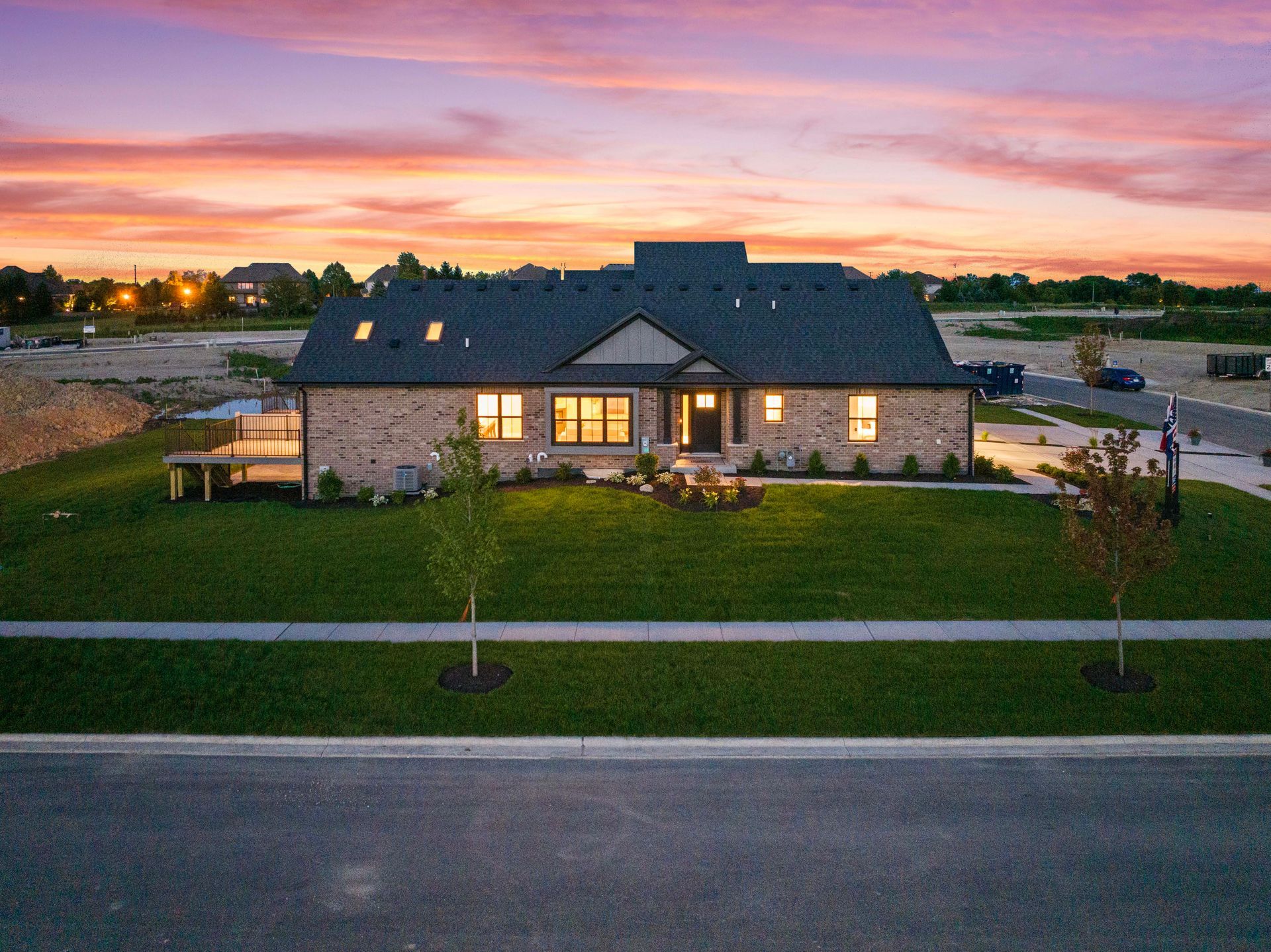 Modern brick home at dusk with warm-lit windows, a landscaped front yard, and a pink sunset sky.