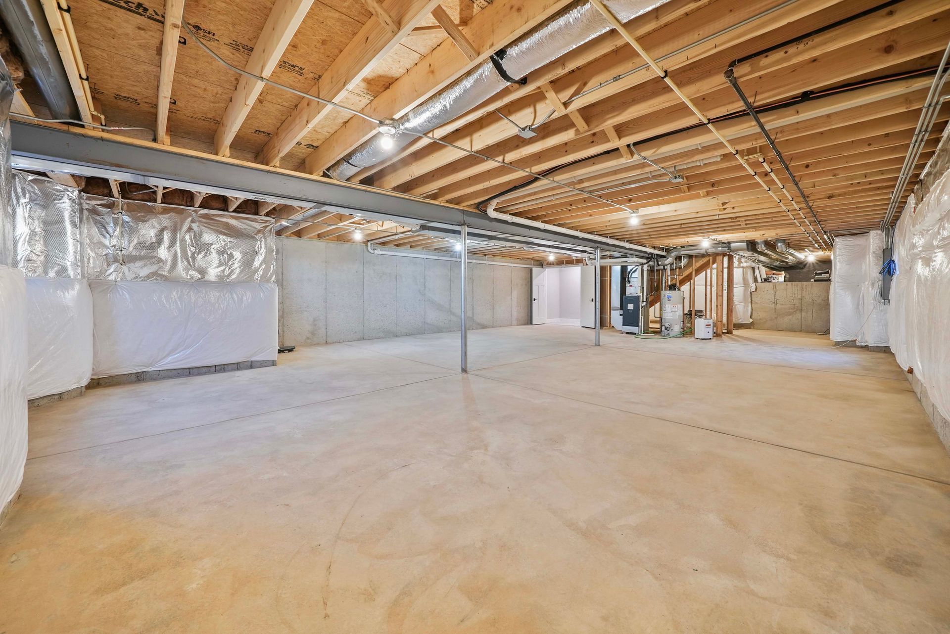 Empty unfinished basement with exposed wooden beams, insulation, and concrete floor
