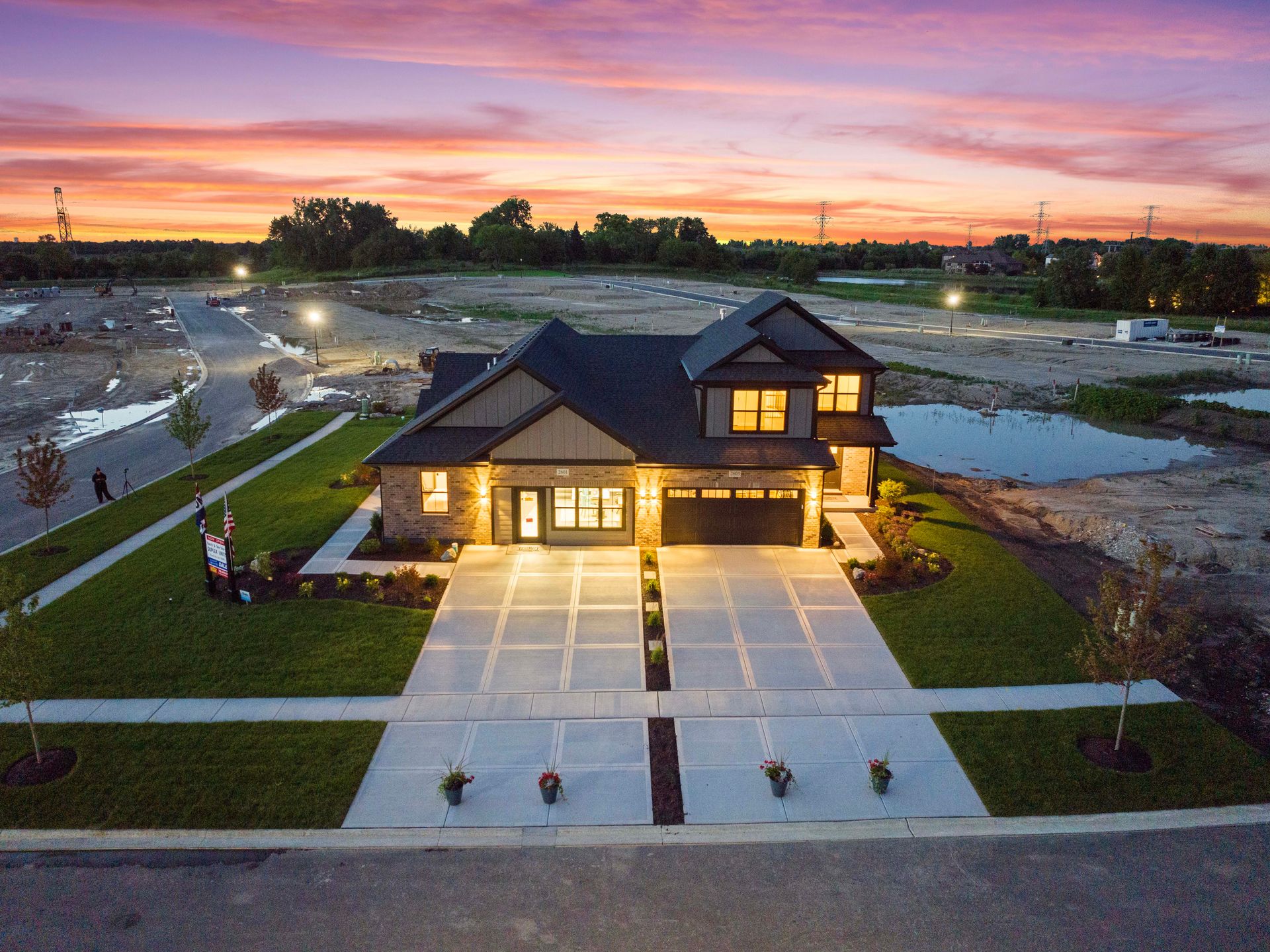 Modern house at sunset with lit windows, long driveway, and landscaped front yard