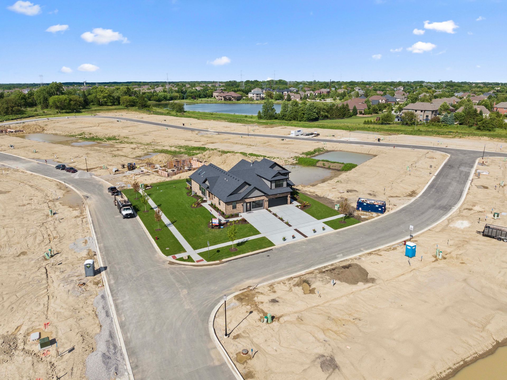 Aerial view of a new house on a corner lot in a suburban housing development with surrounding vacant lots.