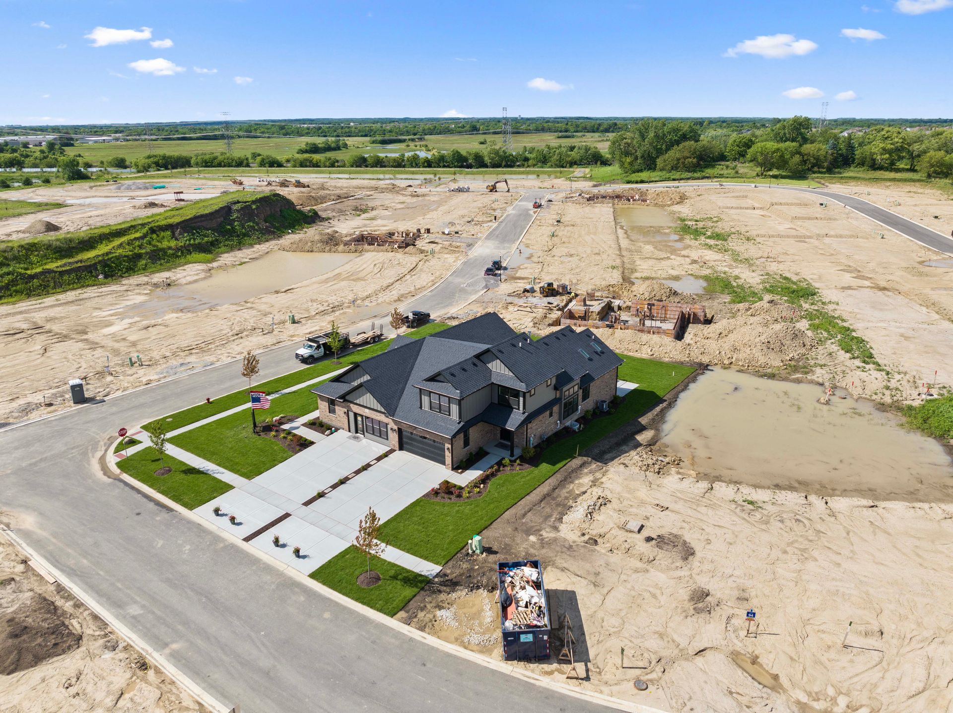 Aerial view of a new house under construction amid a cleared residential lot with roads and landscaping