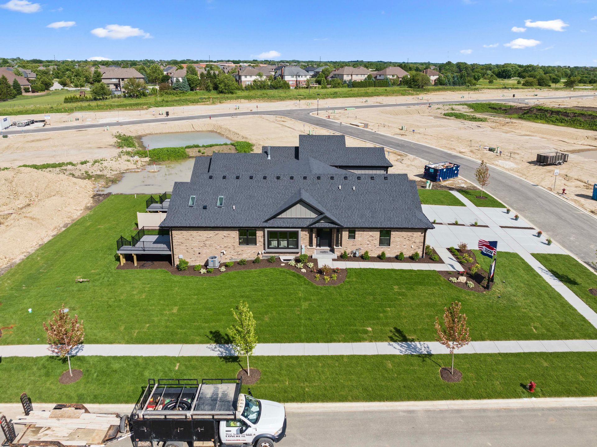 Aerial view of a large brick house with a black roof, green lawn, and construction sites nearby.