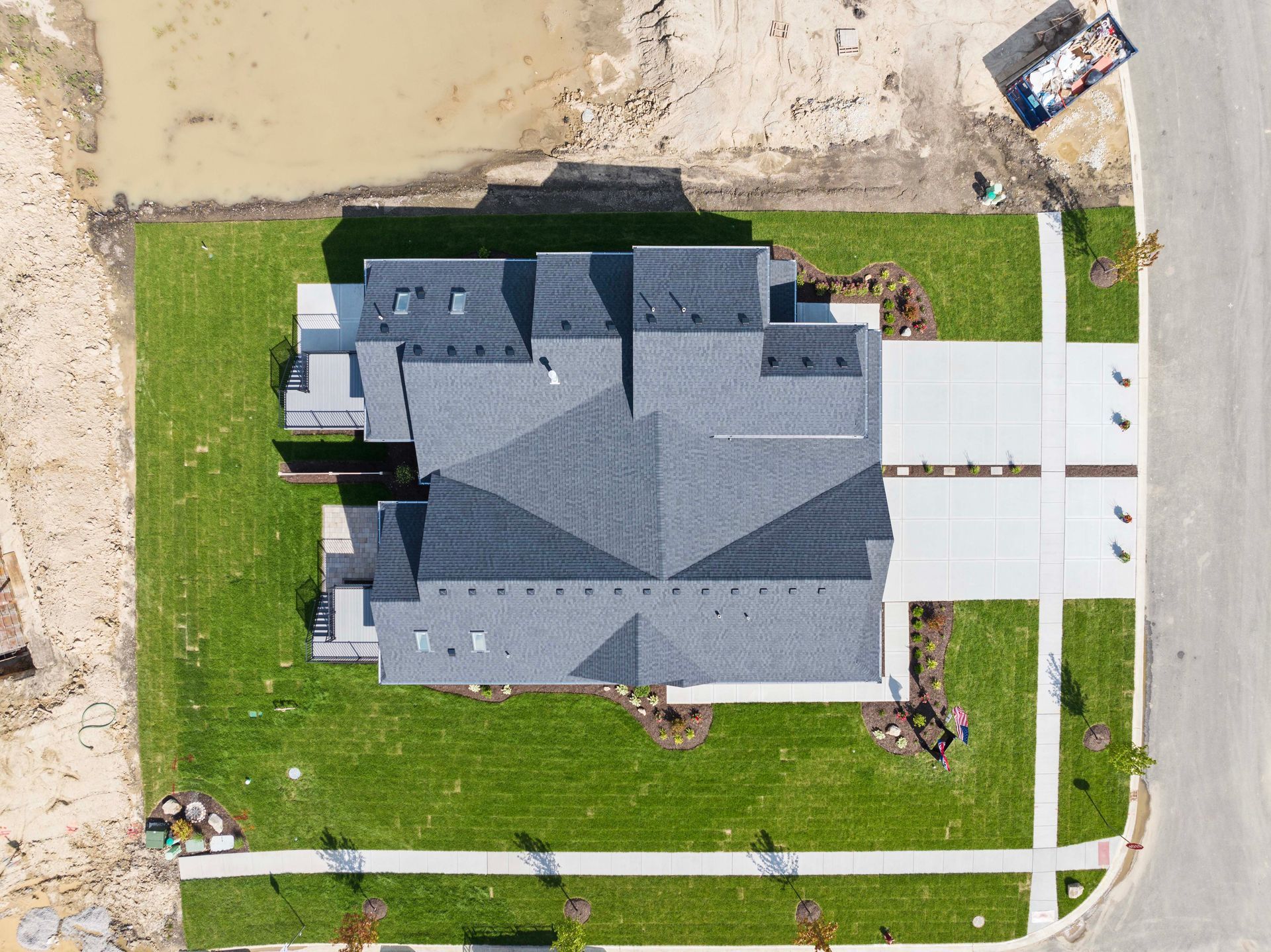 Aerial view of a gray-roofed house with a white driveway and green lawn in a suburban neighborhood