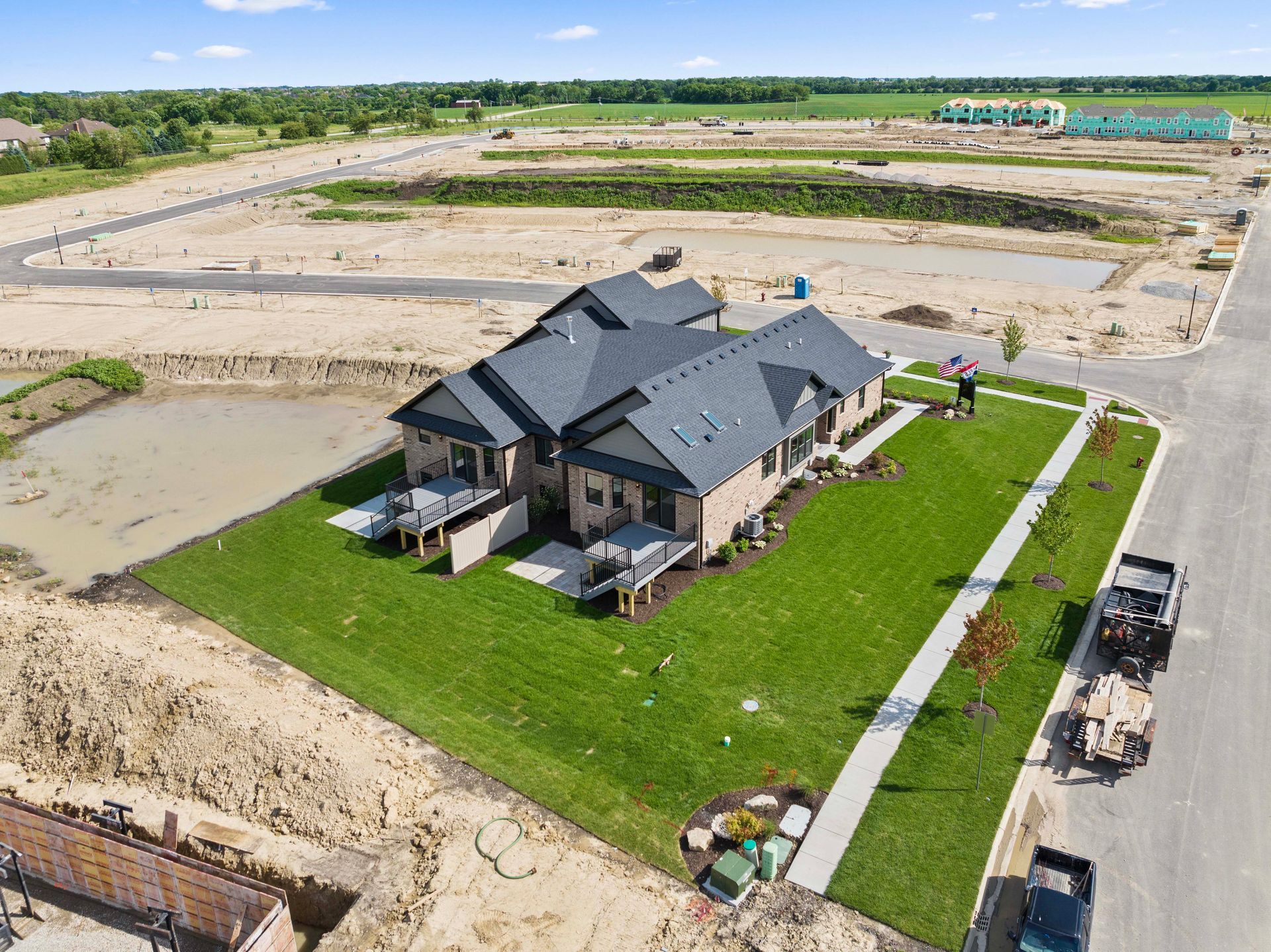 Aerial view of a new black-roofed house on a green lot amid a large construction site