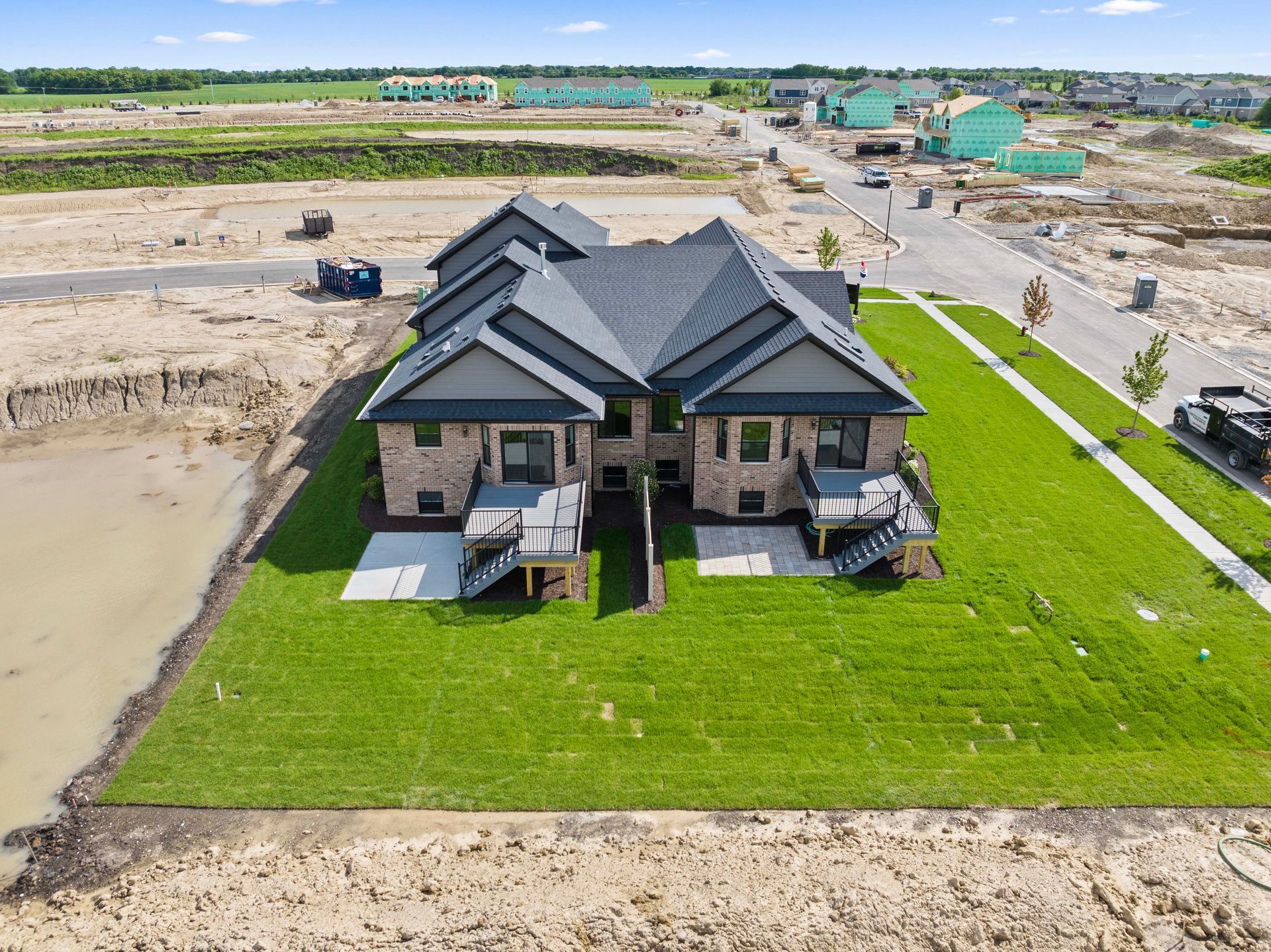 Aerial view of a modern house with a dark roof, green lawn, and nearby construction site.