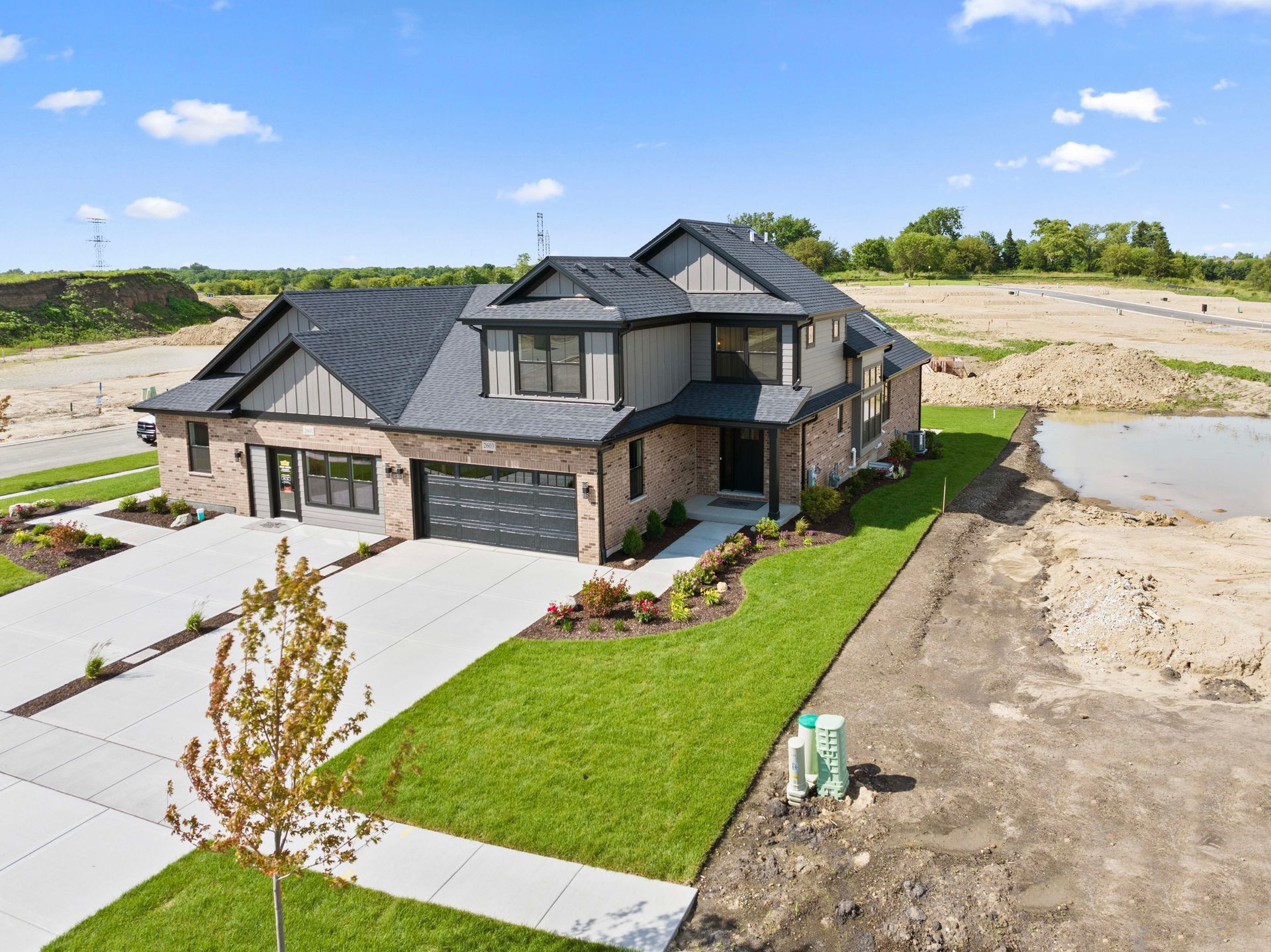 Modern two-story house with gray roof, stone exterior, and manicured lawn in a new residential area