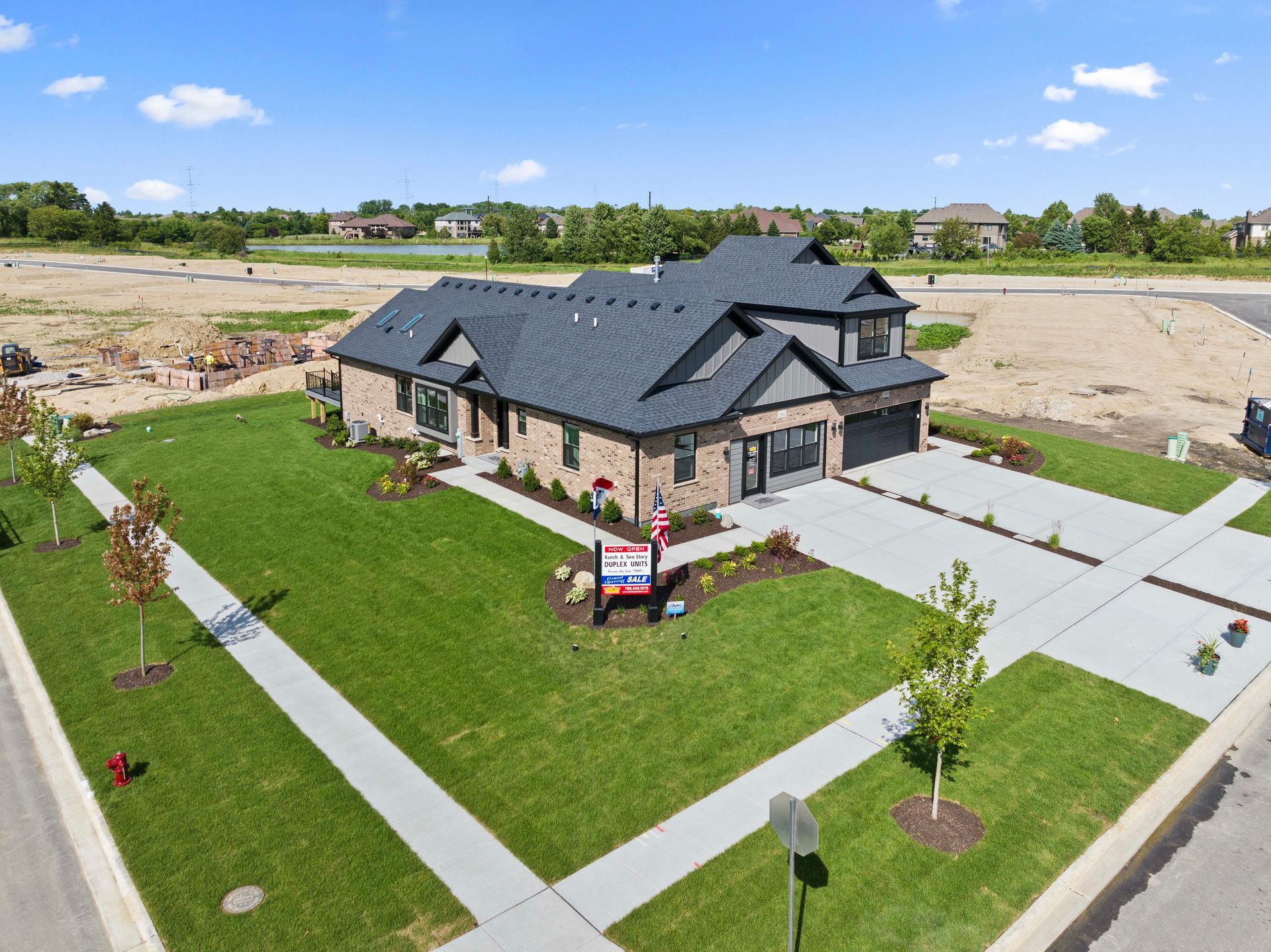 Aerial view of a modern brick house with a dark roof, green lawn, and newly paved driveway in a suburban area