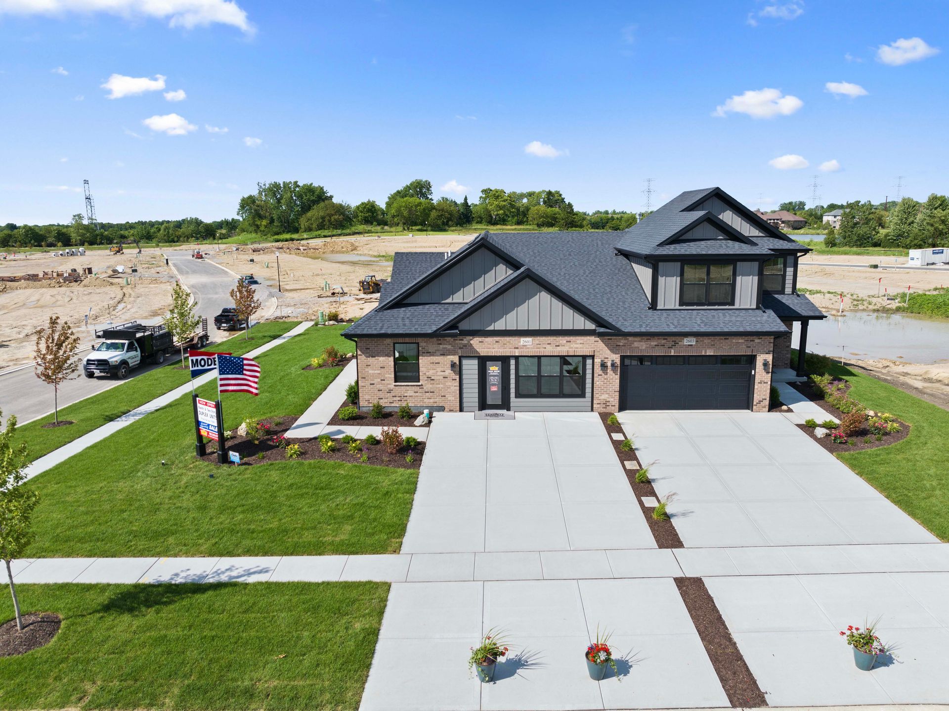 Modern two-story house with gray roof, wide driveway, and American flag in a new neighborhood