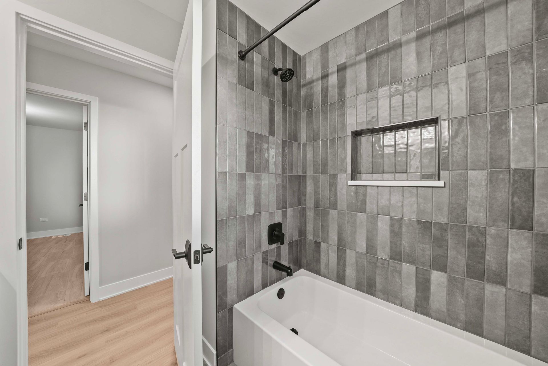 Bathroom with gray tile shower and white bathtub, viewed through an open door from a hallway