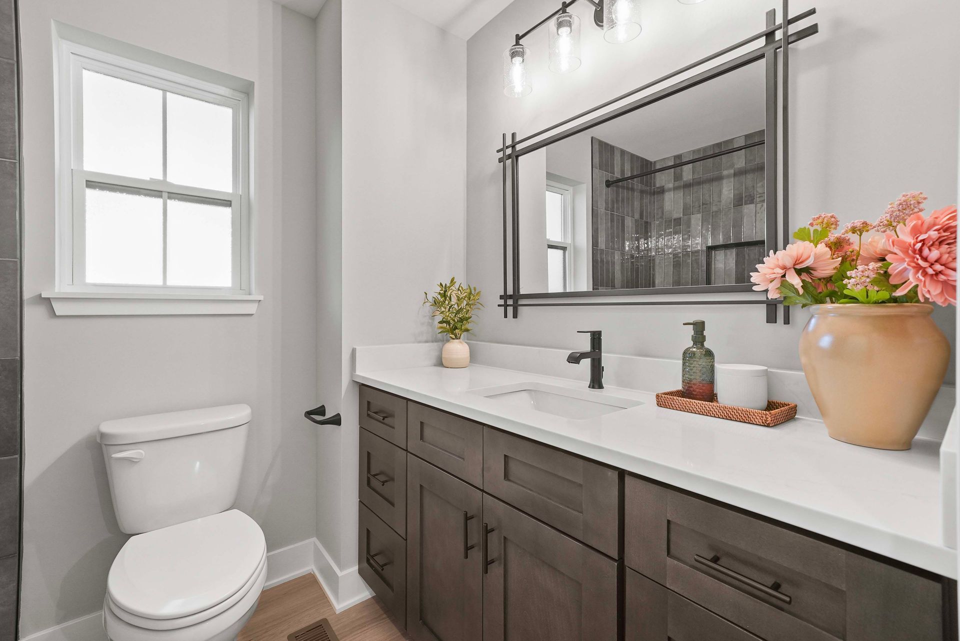 Small bathroom with a toilet, dark vanity, white countertop, and a mirror above it.