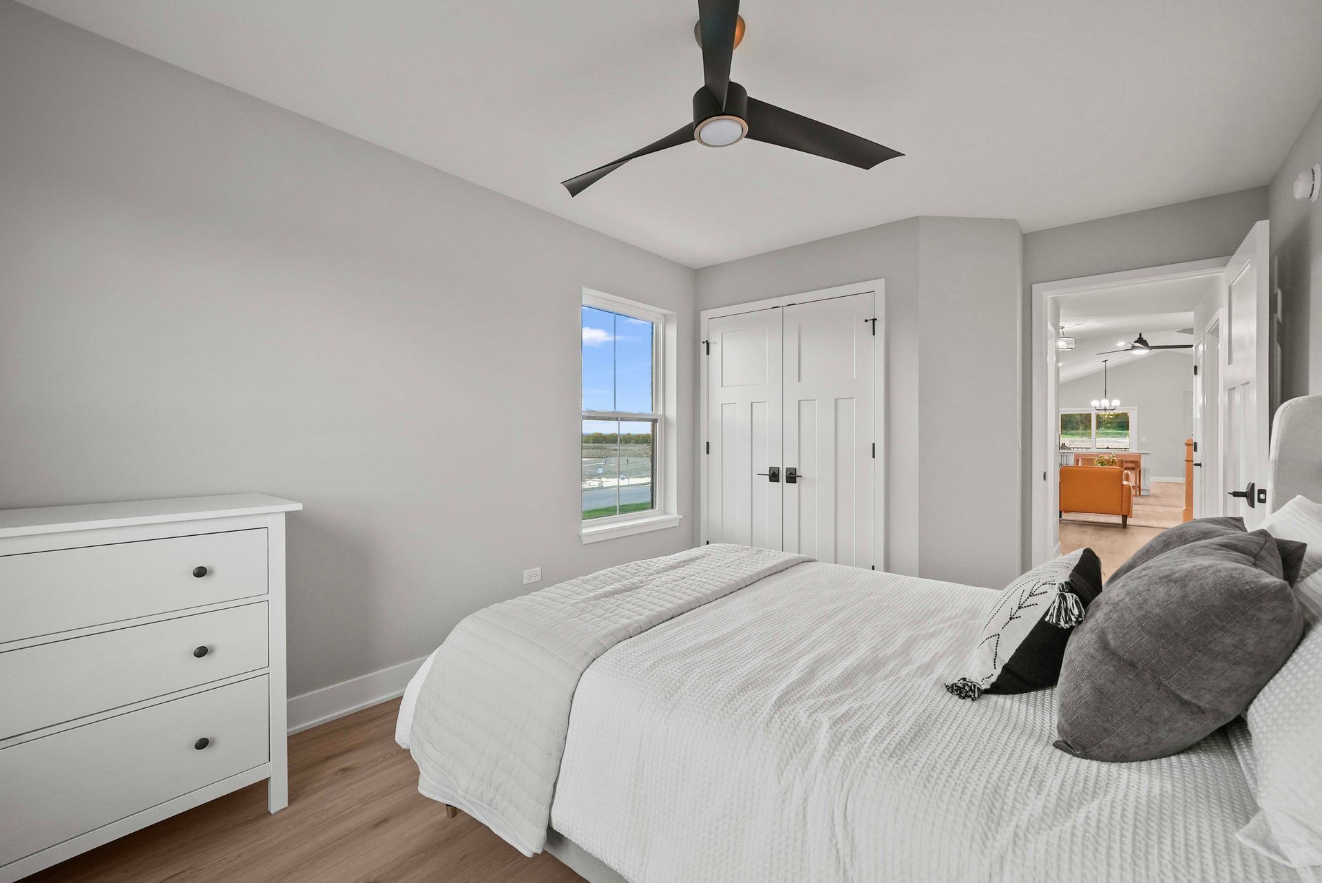 Bright bedroom with white bed, dresser, closet doors, window, and ceiling fan
