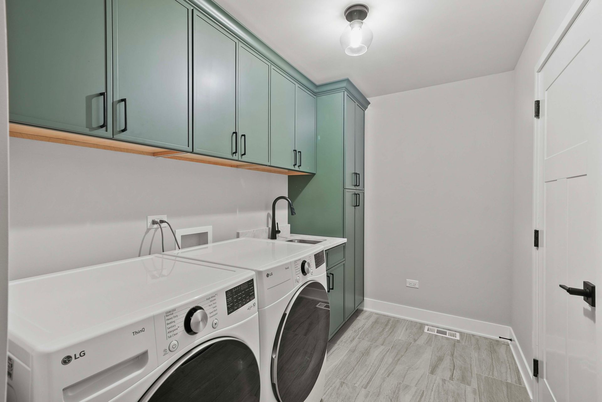 Laundry room with white washer and dryer, sage green cabinets, sink, and gray floor.