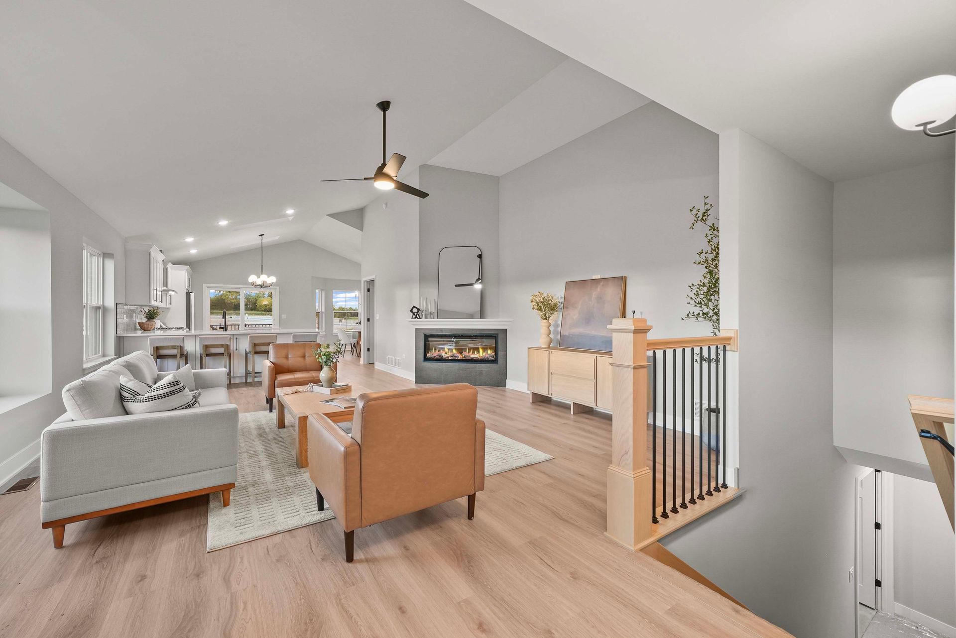 Bright open living room with gray sofas, tan chairs, fireplace, wood floors, and a ceiling fan
