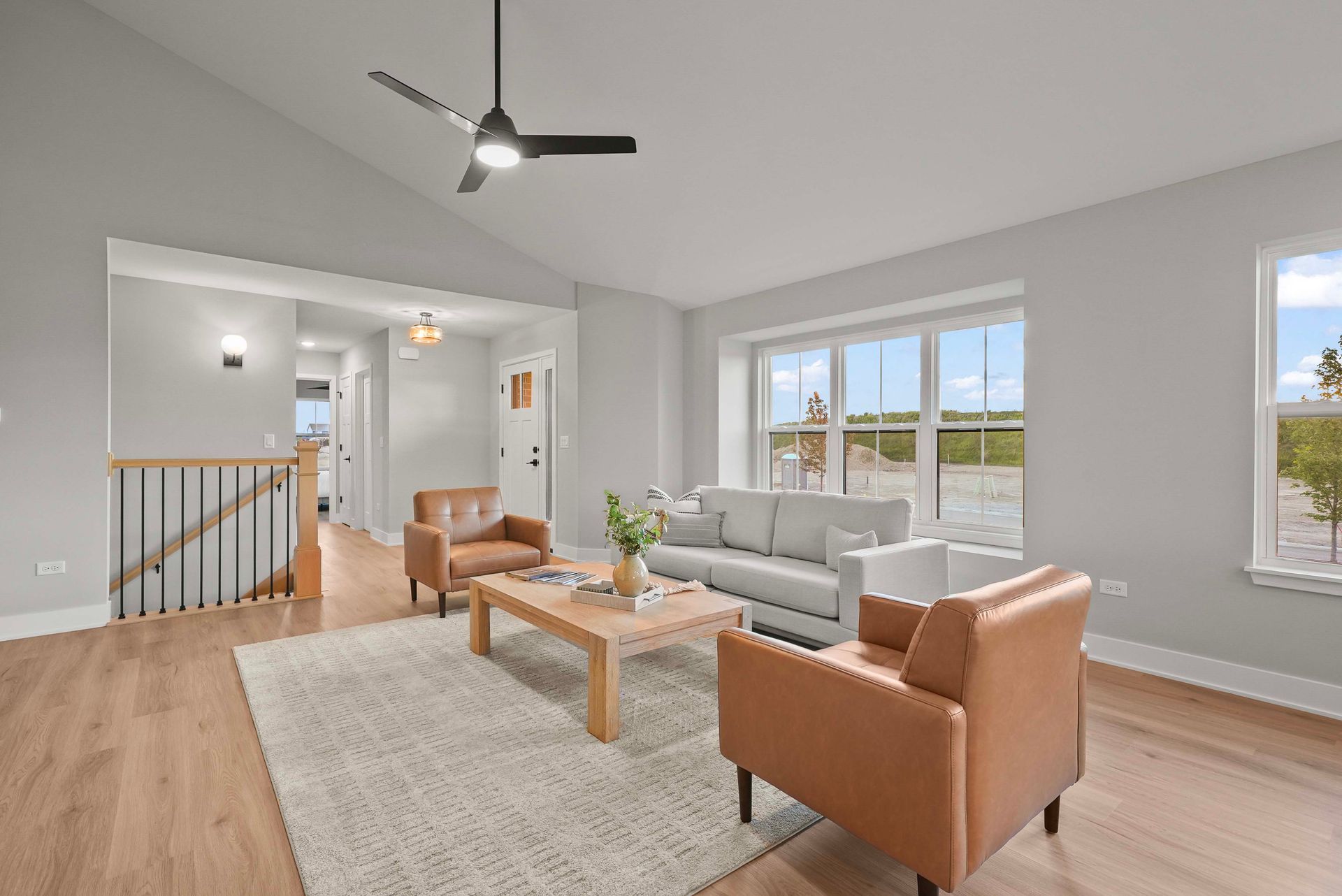 Bright open living room with gray sectional, tan chairs, wooden table, and large windows.